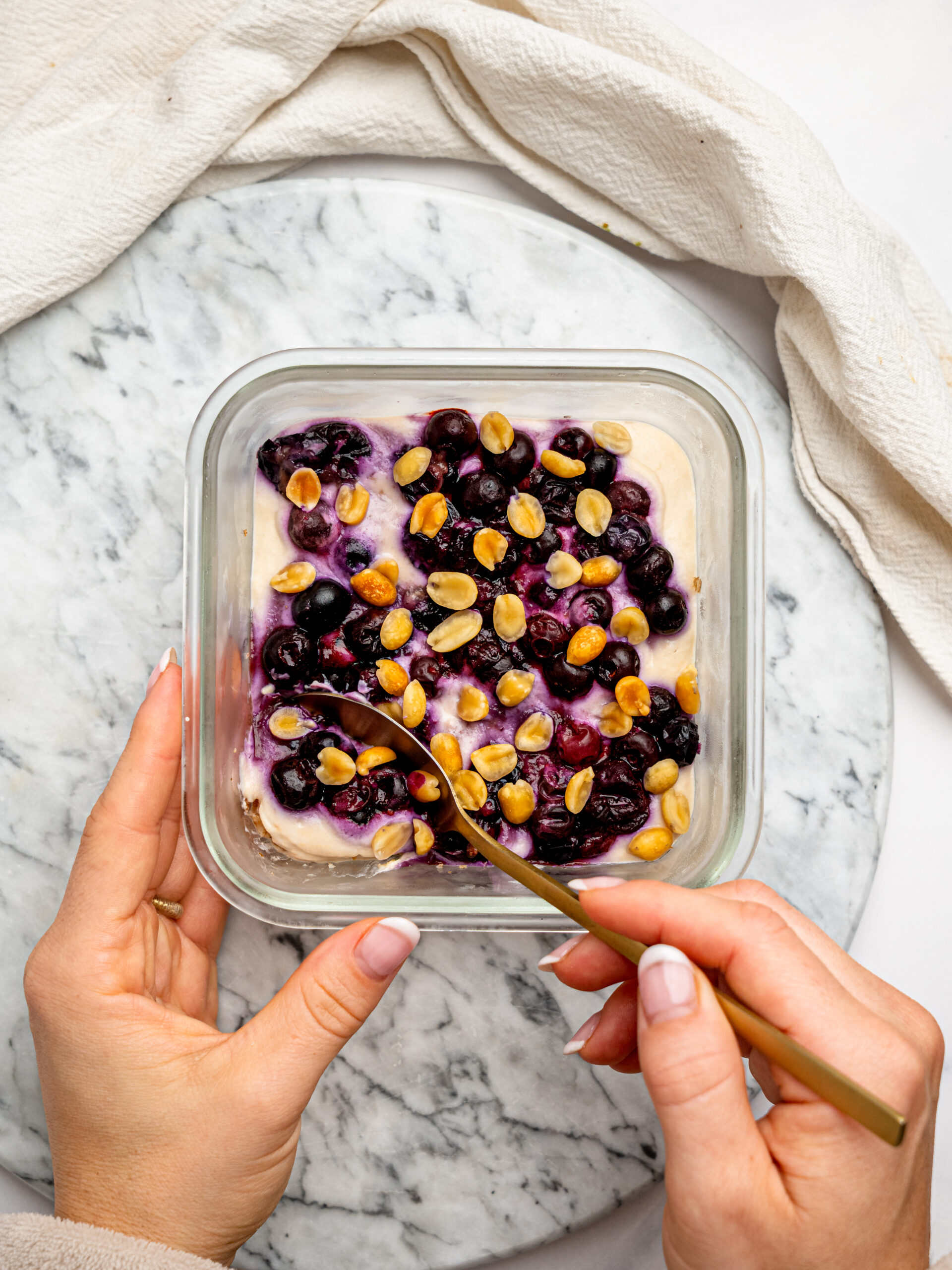 Hands holding a glass container of PB&J Overnight Weetbix topped with jammy berries and crunchy peanuts.