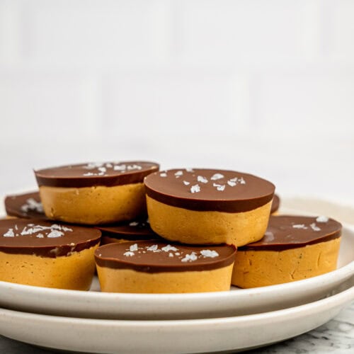 Close-up of protein peanut butter cups layered with a thick peanut butter filling and dark chocolate topping, garnished with flaky sea salt.