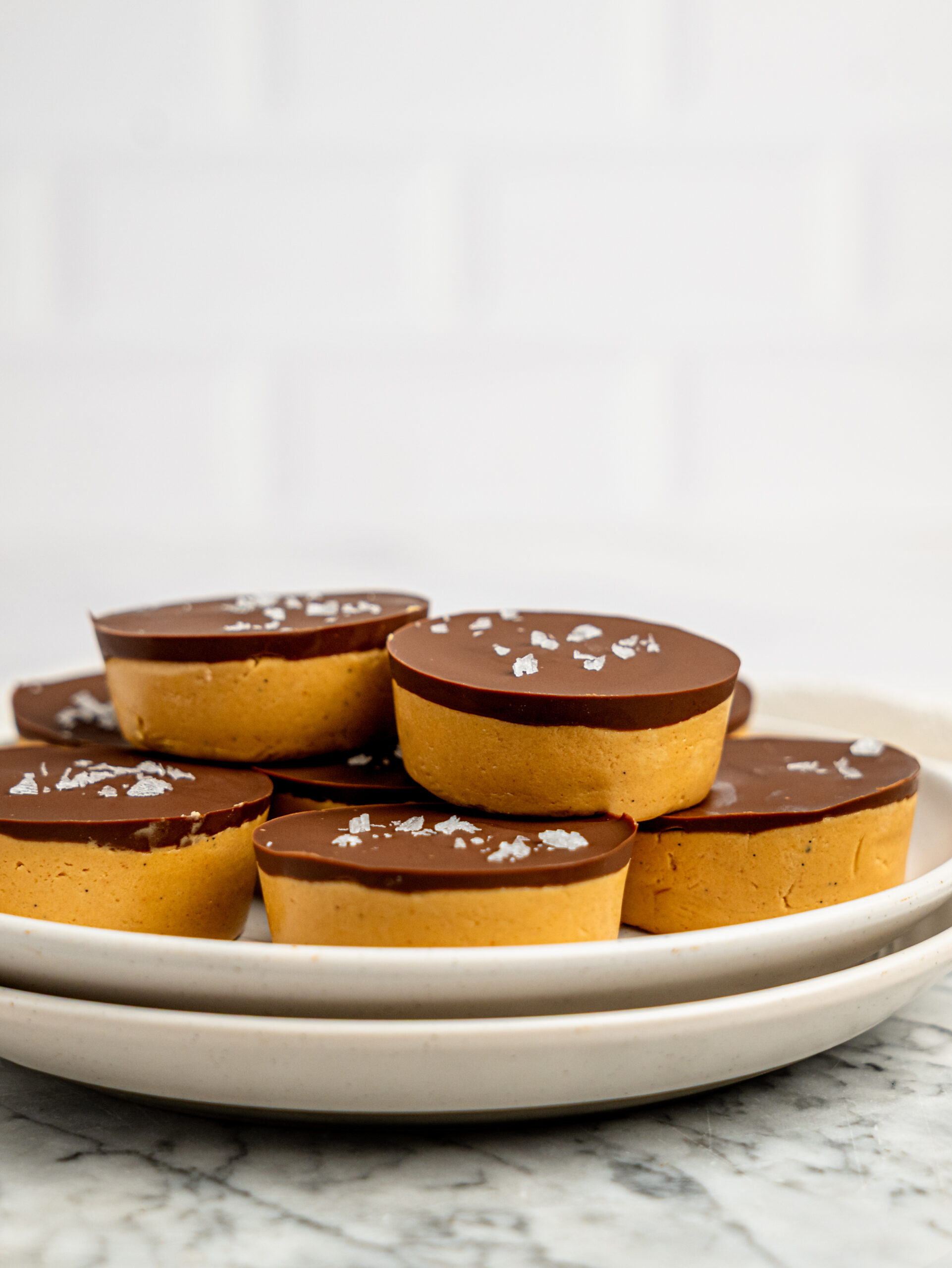 Close-up of protein peanut butter cups layered with a thick peanut butter filling and dark chocolate topping, garnished with flaky sea salt.