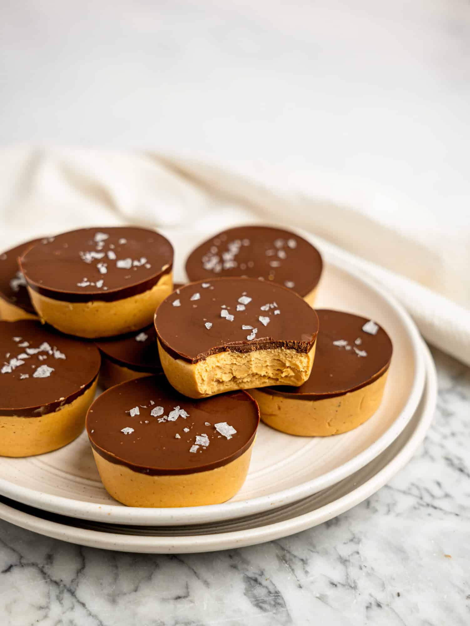 Protein peanut butter cups arranged on white plates, with one cup cut in half to showcase the creamy, high-protein peanut butter centre and dark chocolate layer.