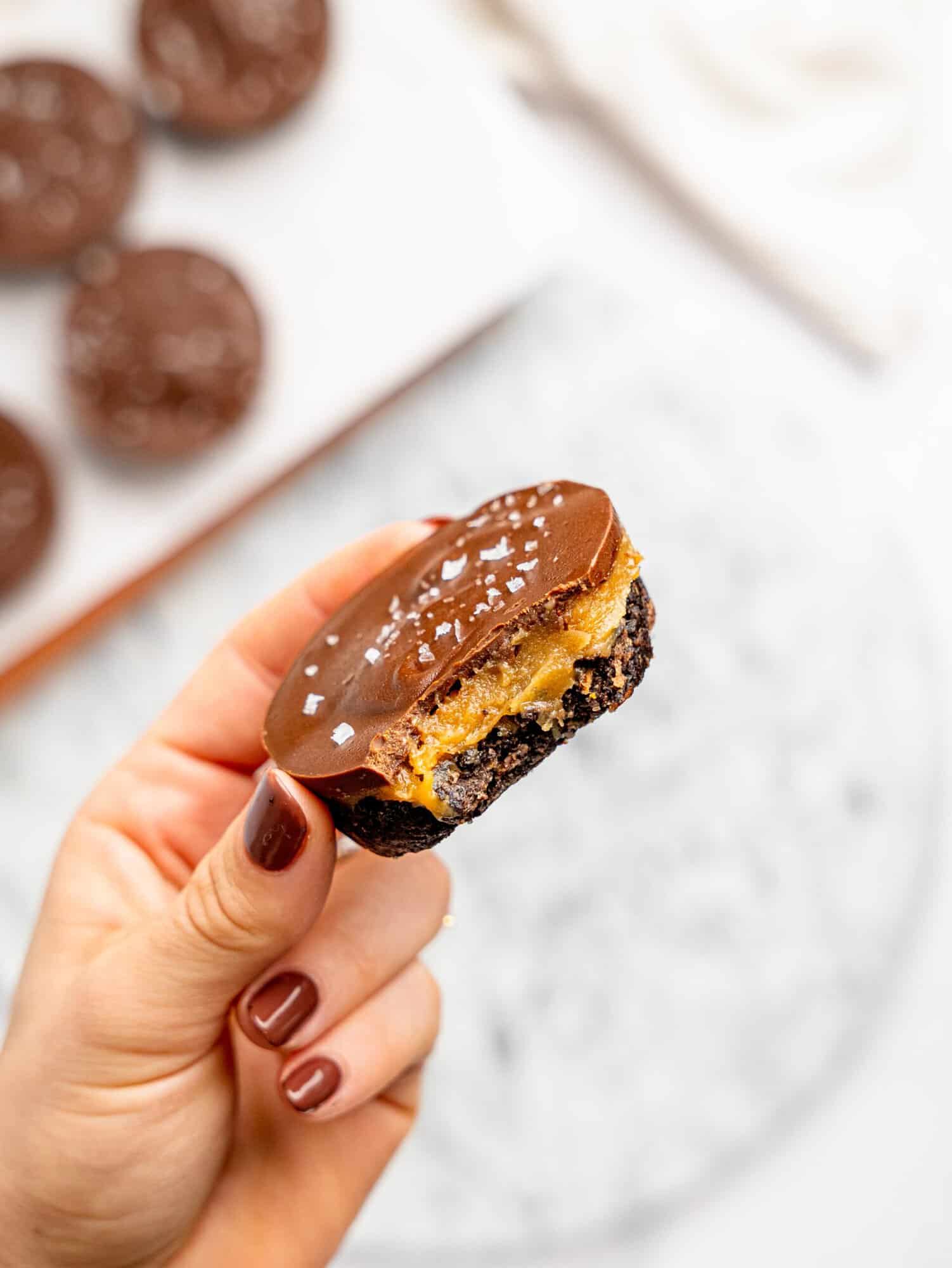 Hand holding a bitten No-Bake Snickers Weetbix Cup with chocolate topping, creamy peanut butter filling, and flaky sea salt.