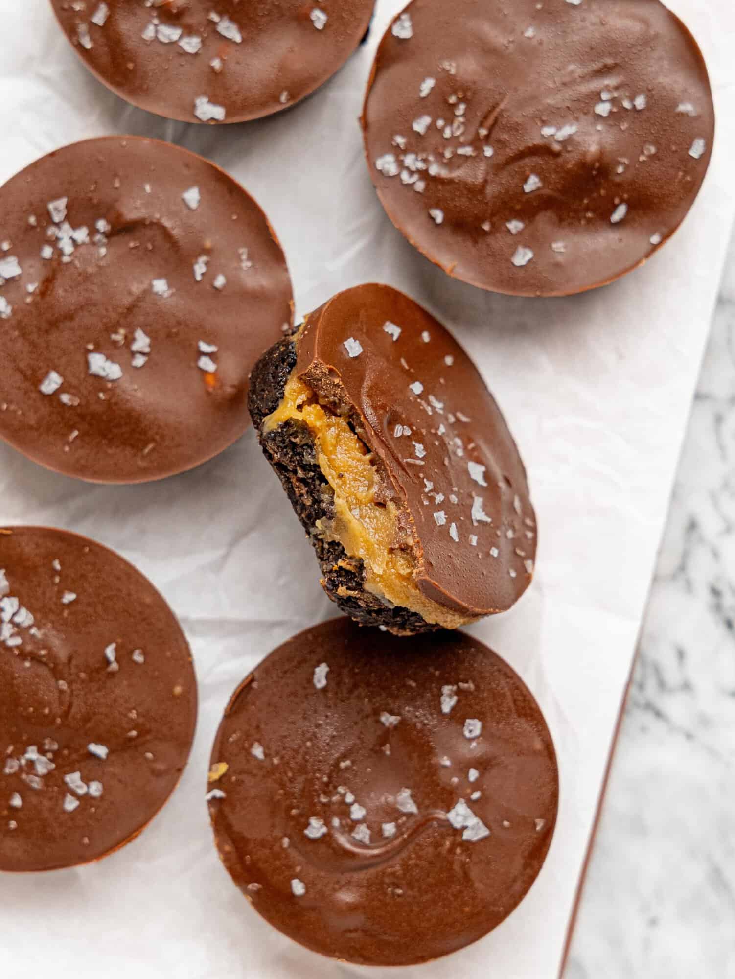 Overhead view of No-Bake Snickers Weetbix Cups topped with dark chocolate and sea salt, with one cup cut open to show the layers.