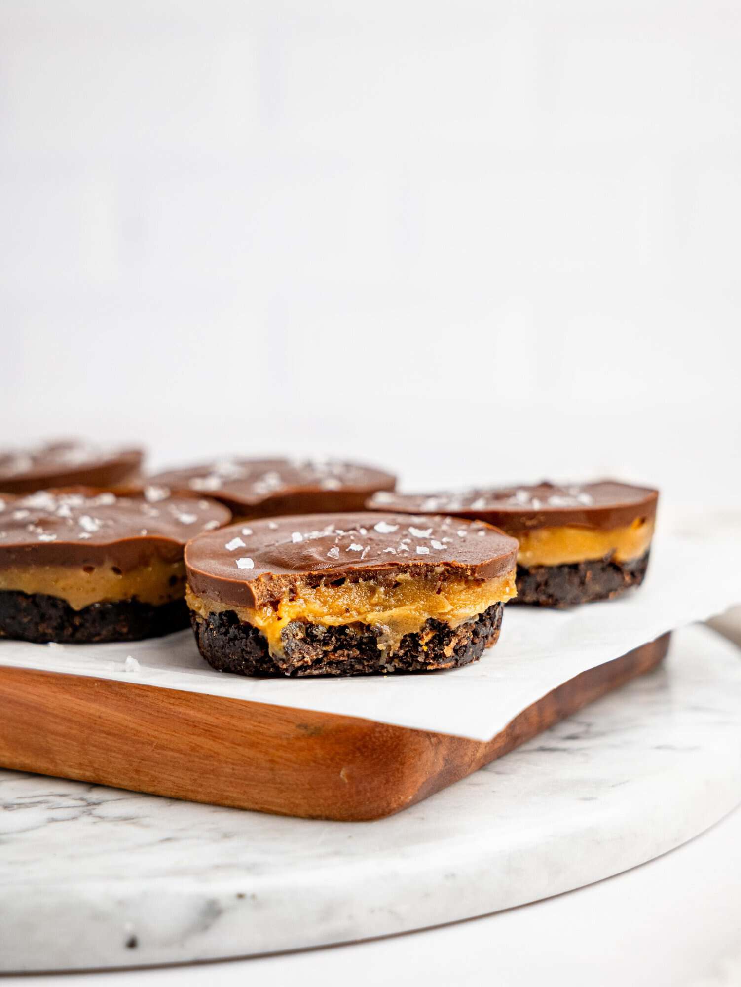 Side view of layered Snickers Weetbix Cups on a wooden board, featuring a chocolate Weetbix base, peanut butter filling, and chocolate topping.