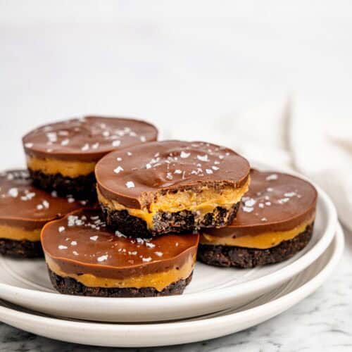 Stacked No-Bake Snickers Weetbix Cups on white plates with a visible peanut butter center and dark chocolate coating.