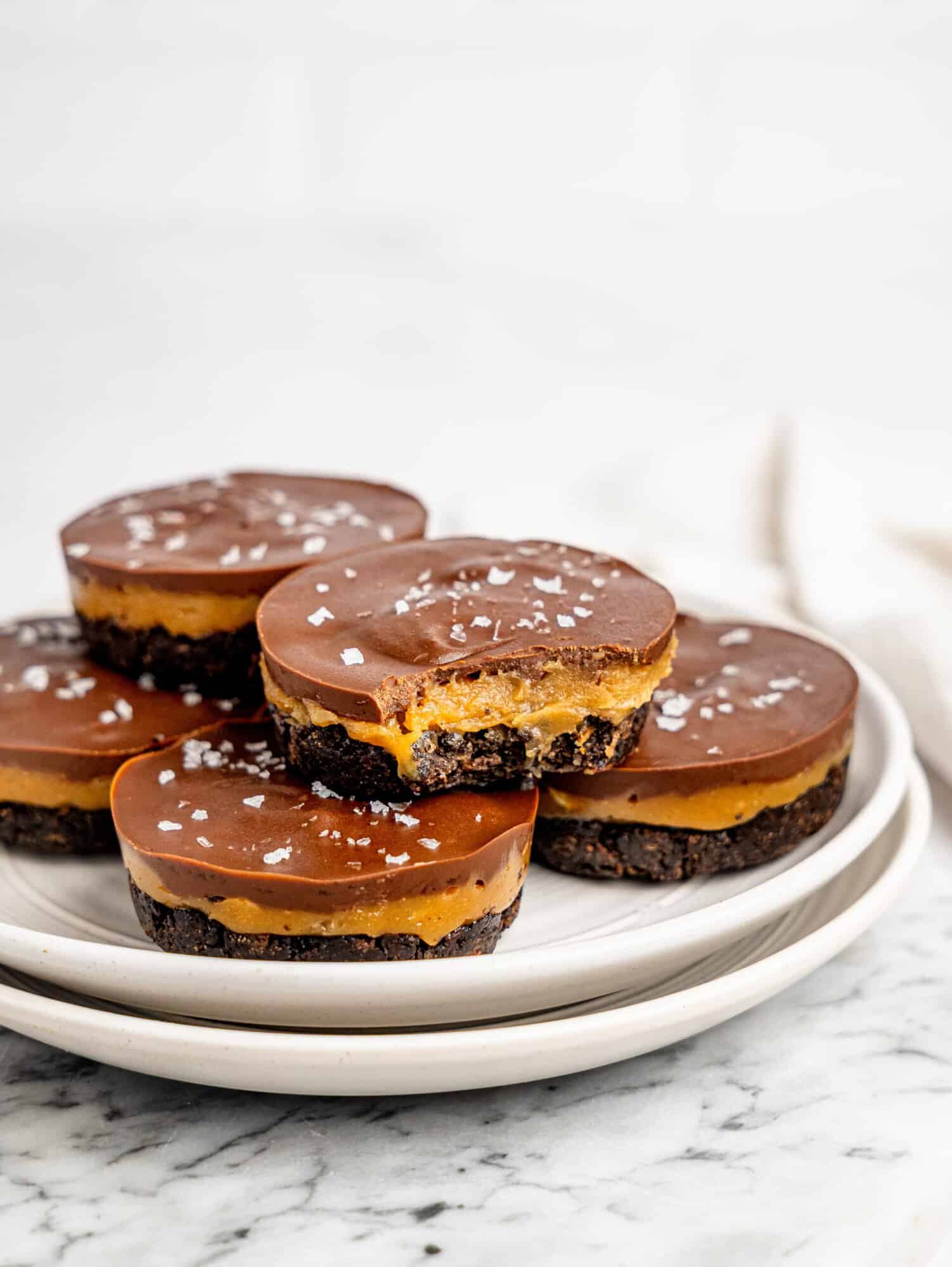 Stacked No-Bake Snickers Weetbix Cups on white plates with a visible peanut butter center and dark chocolate coating.