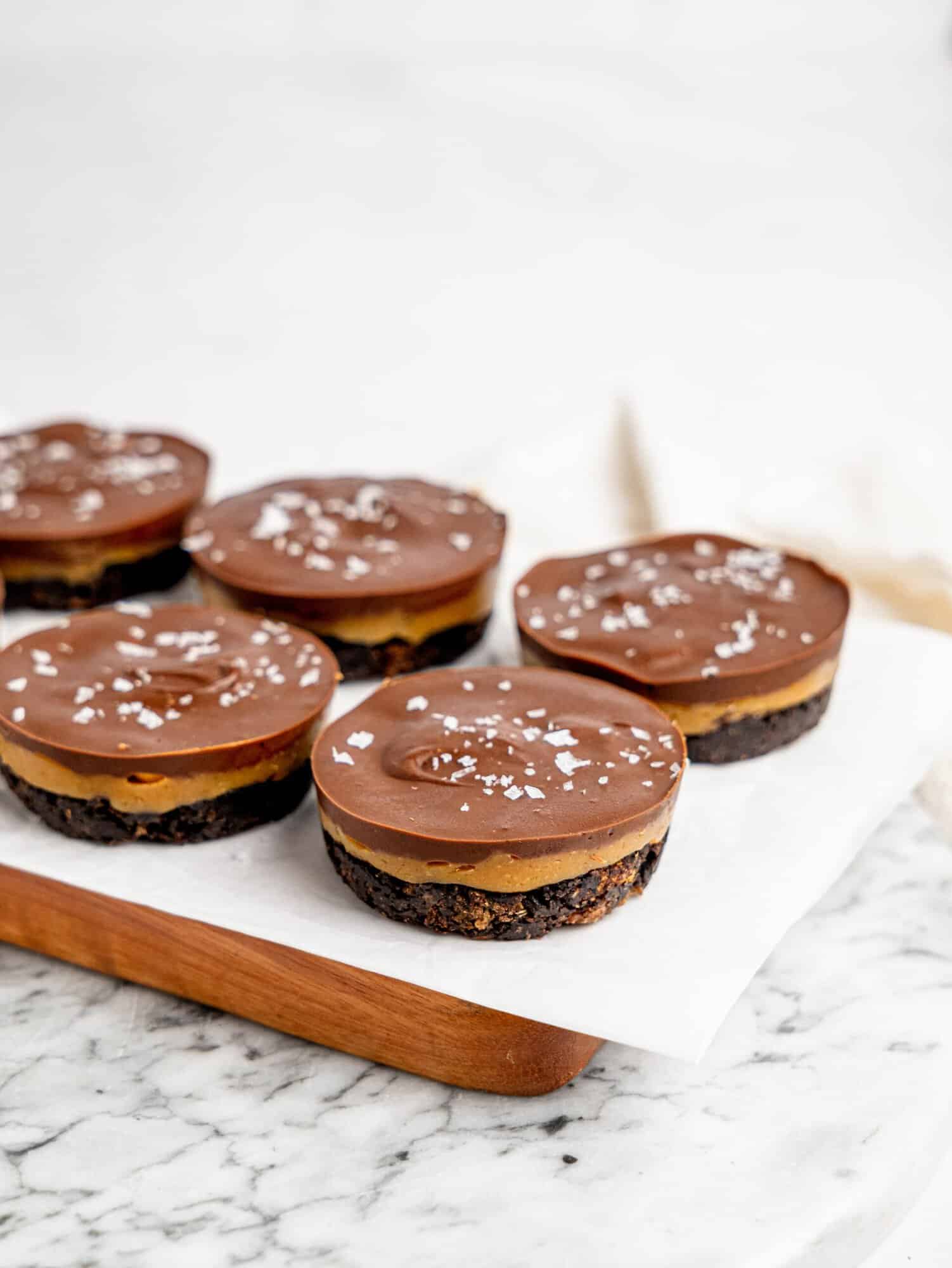 No-Bake Snickers Weetbix Cups displayed on a wooden serving board with smooth chocolate tops and creamy peanut butter layers.