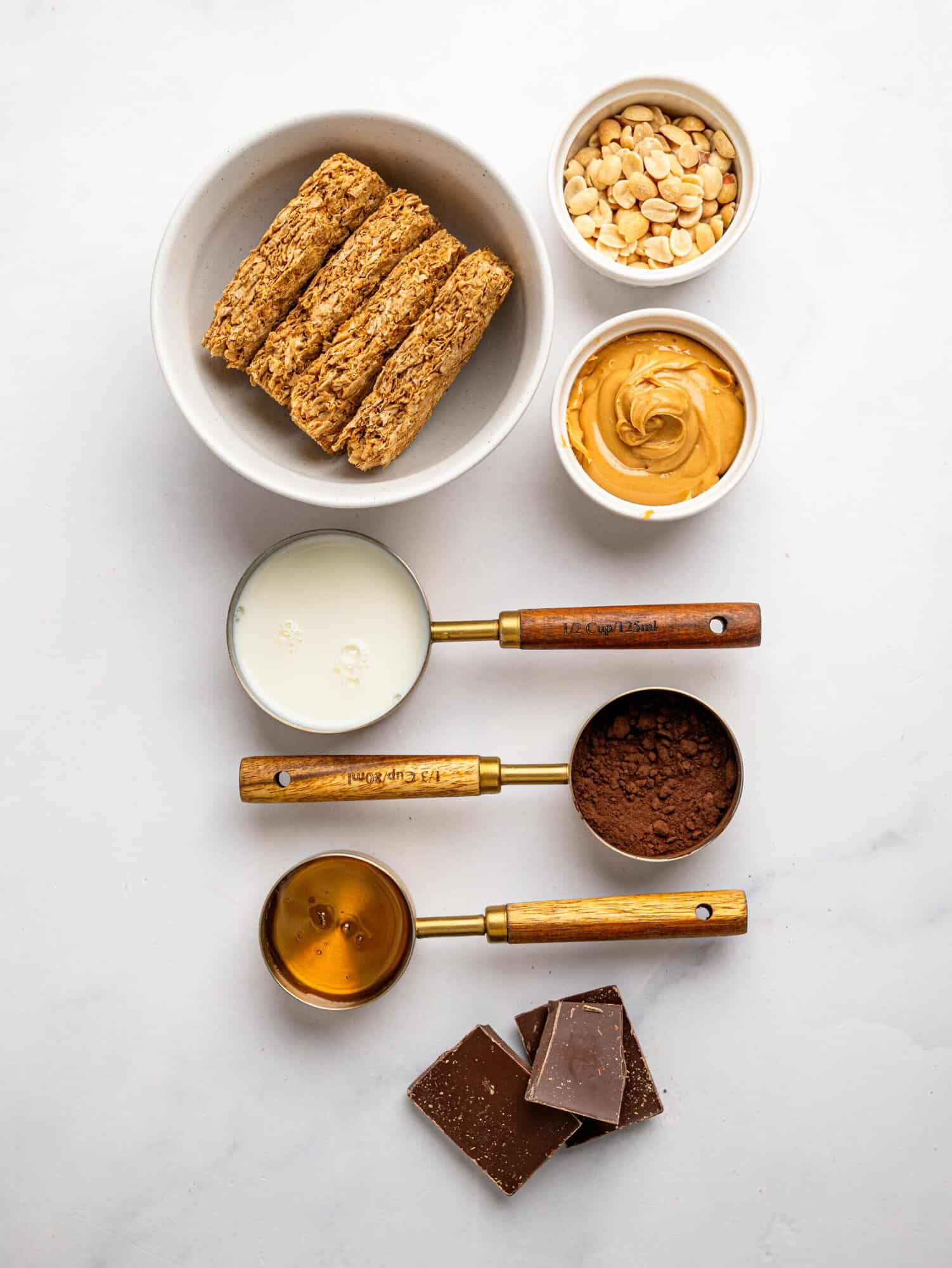 Ingredients for No-Bake Snickers Weetbix Cups including Weetbix, peanut butter, peanuts, milk, cocoa powder, honey, and dark chocolate.