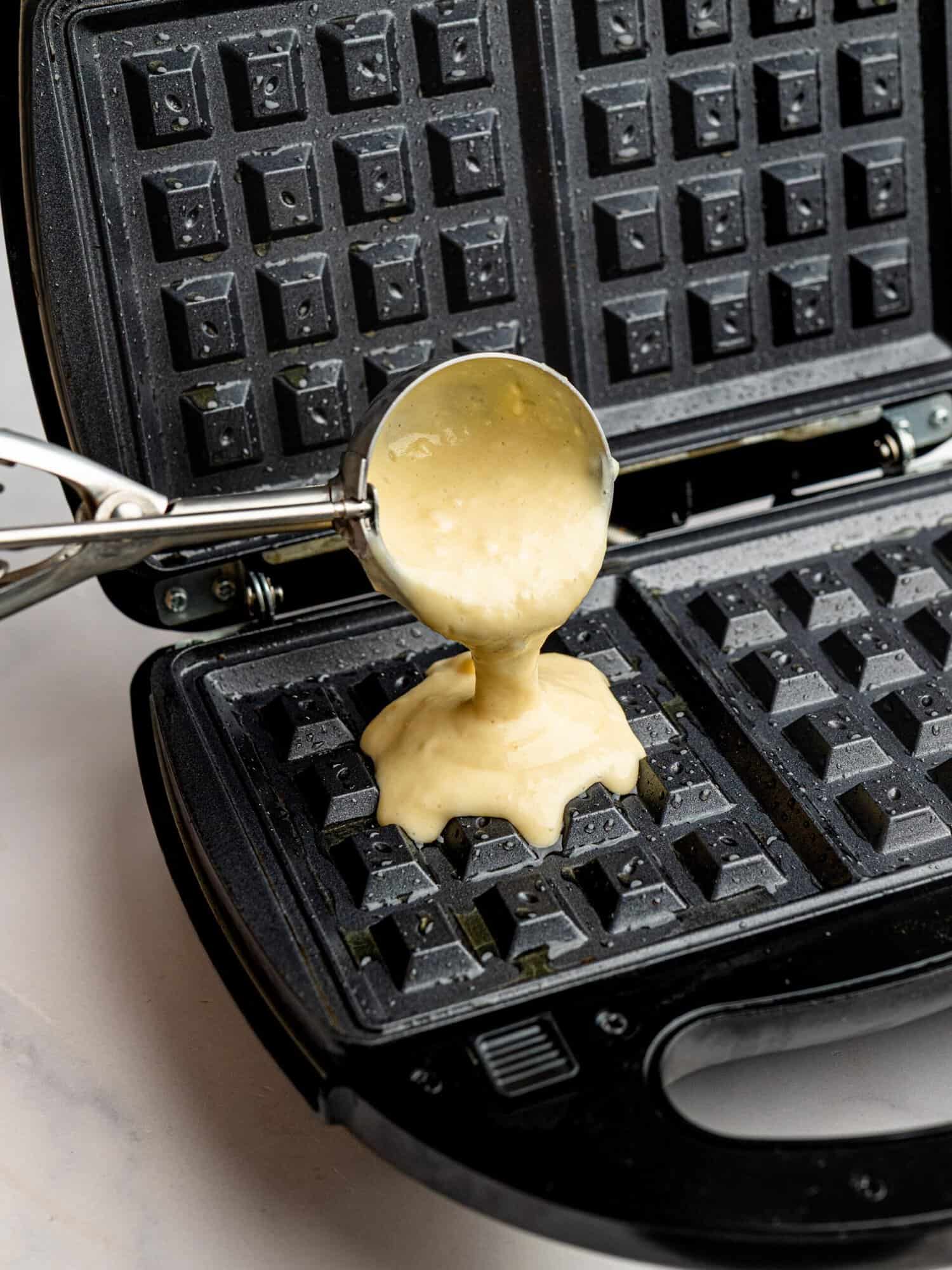 Pouring gluten free waffle batter into a waffle maker for homemade waffles.
