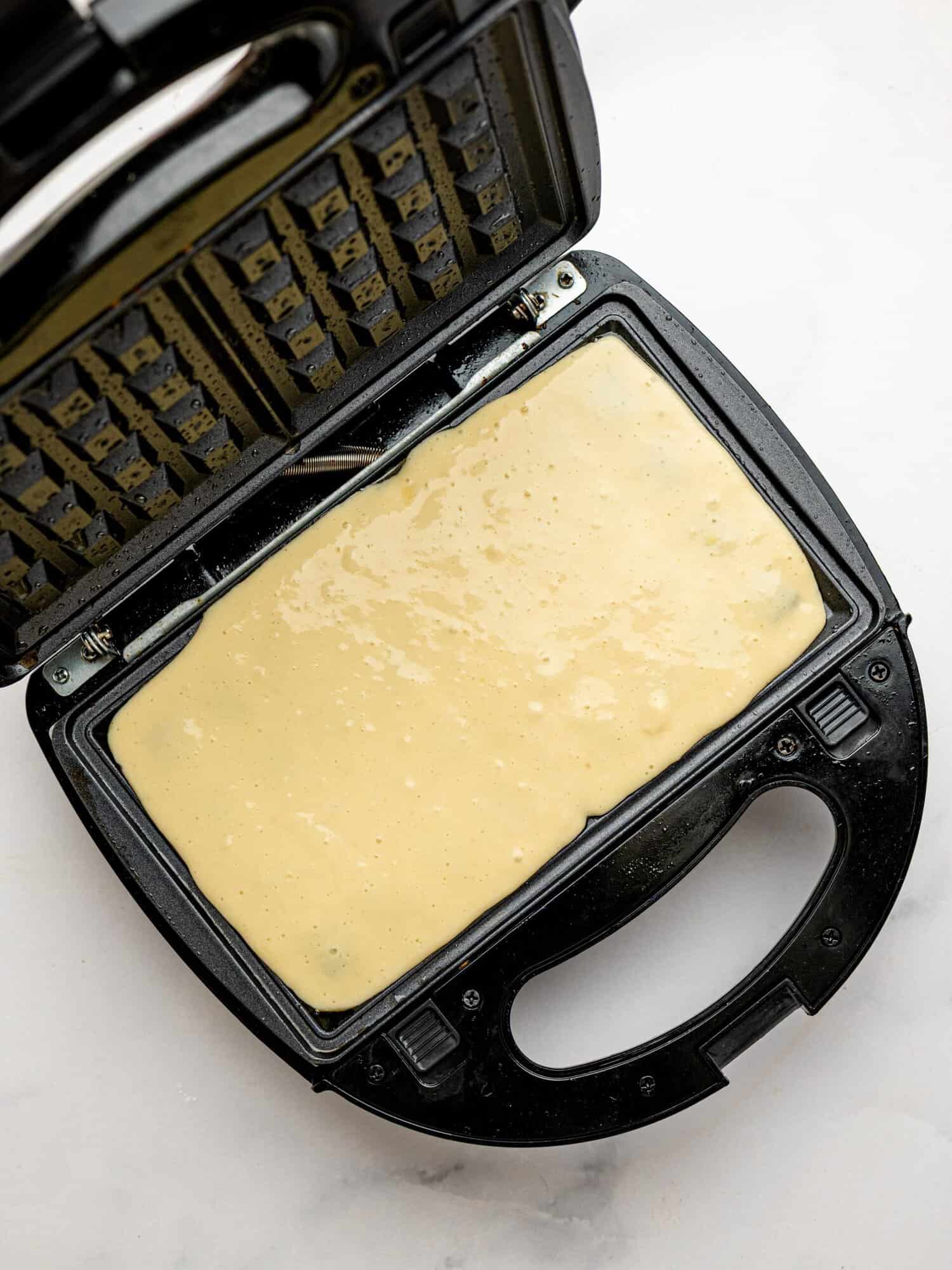 Gluten free waffle batter poured into a preheated waffle maker before cooking.