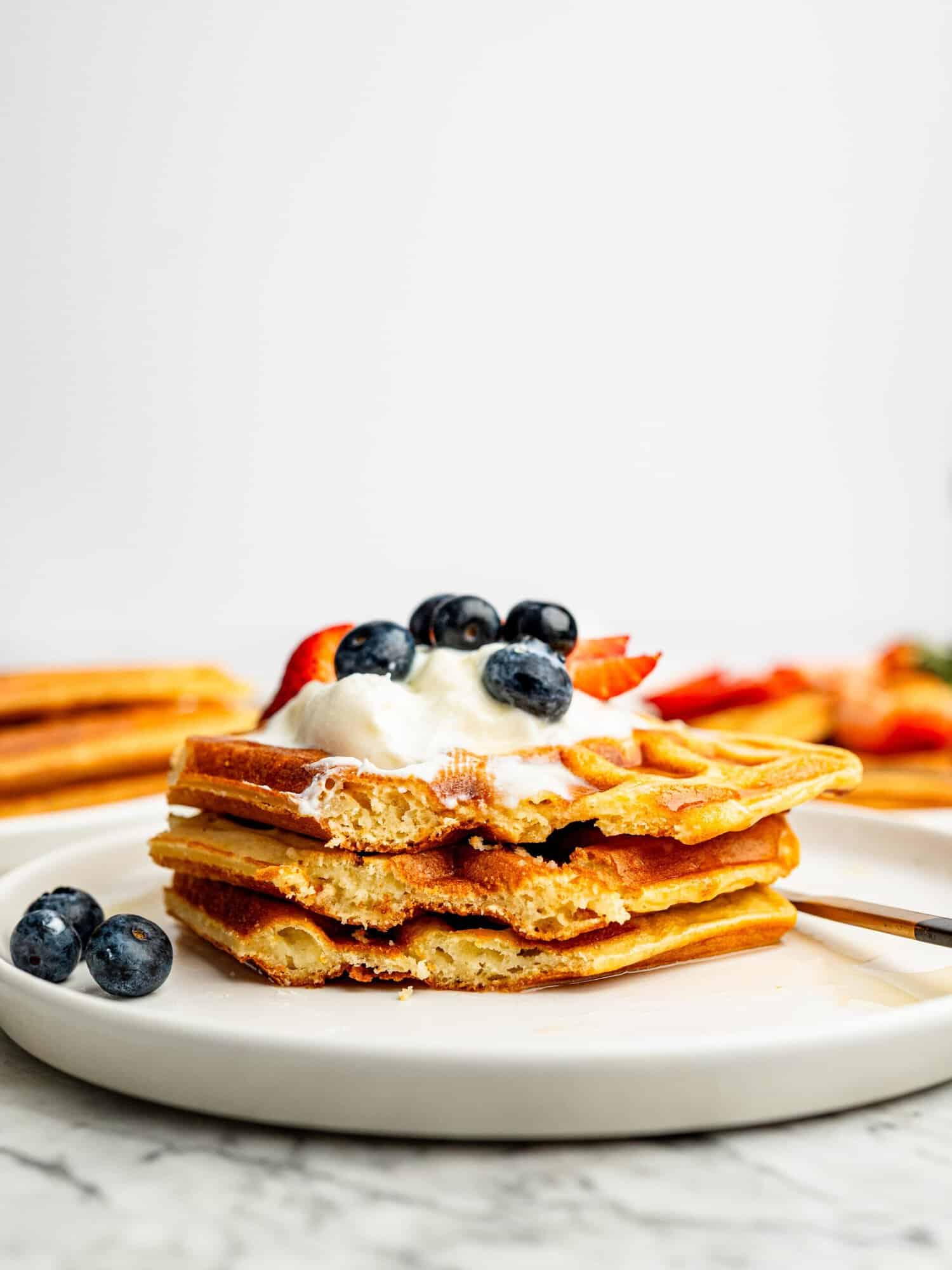 Light and fluffy gluten-free waffles topped with Greek yogurt, blueberries, and strawberries.