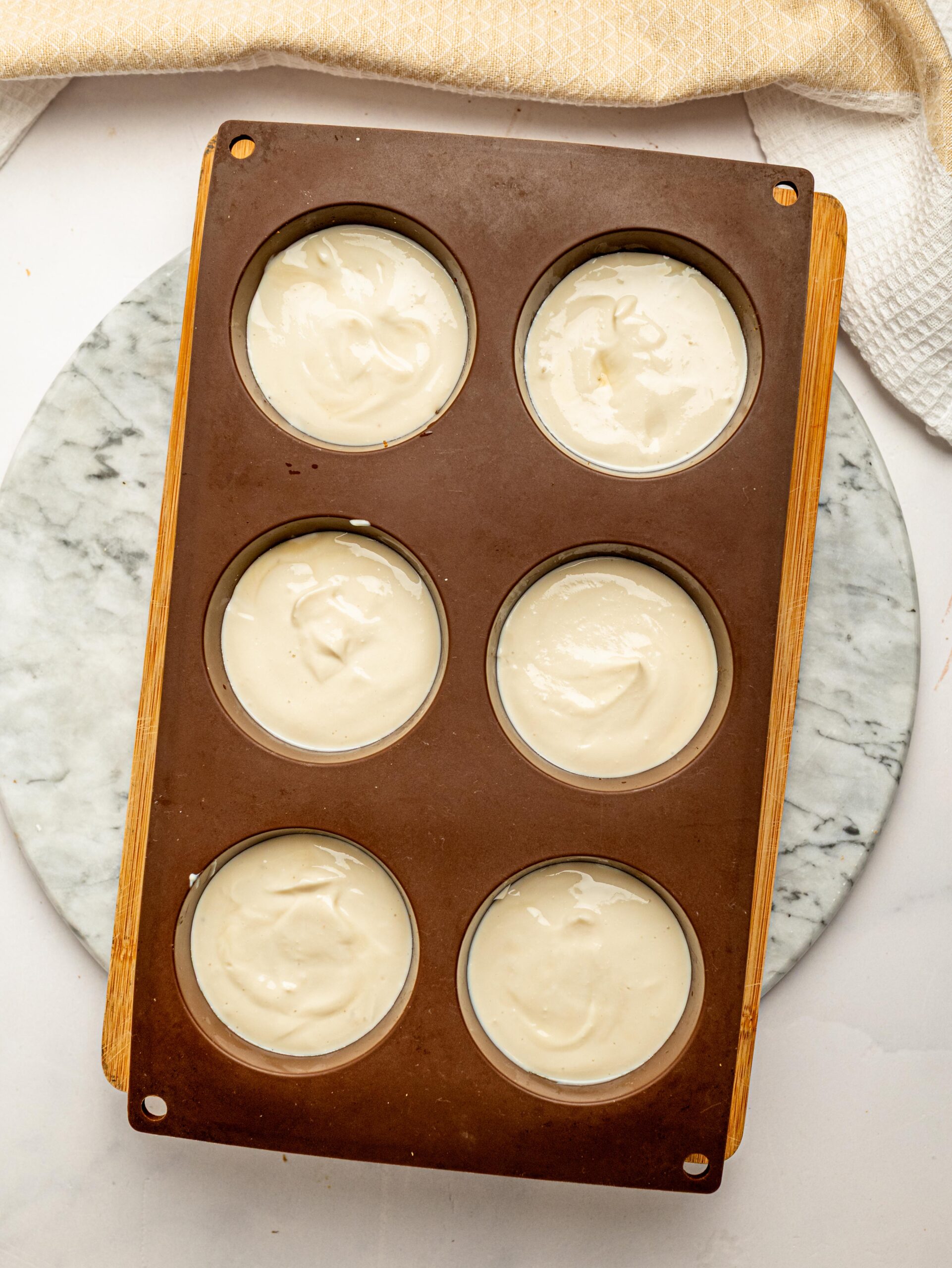 Six Mini Tiramisu Cheesecake Weetbix Cups topped with creamy cheesecake filling in a silicone muffin pan before chilling.