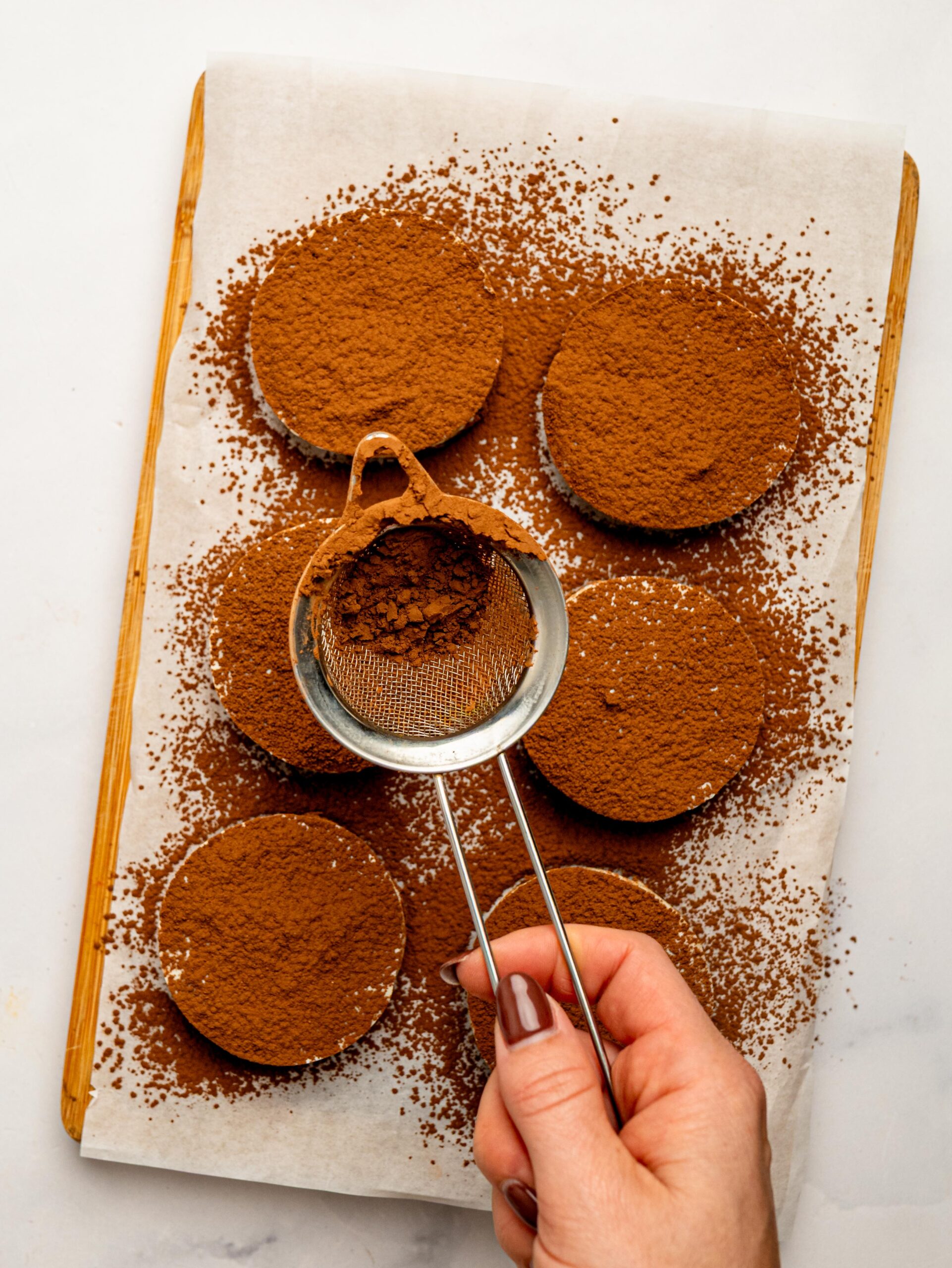 Dusting cocoa powder over Mini Tiramisu Cheesecake Weetbix Cups using a fine mesh sieve.