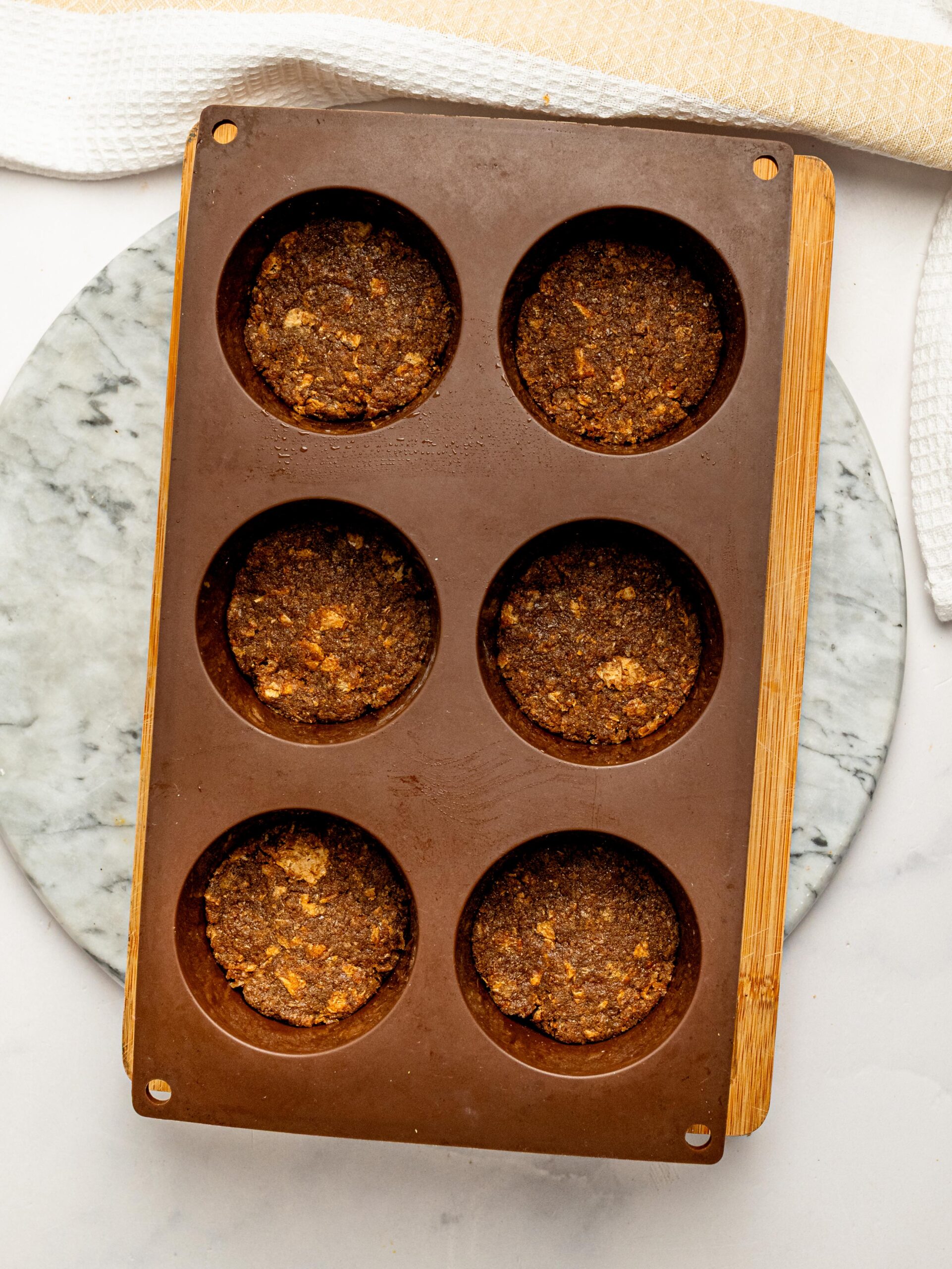 Coffee-infused Weetbix bases pressed firmly into a silicone muffin pan ready for the cheesecake filling.