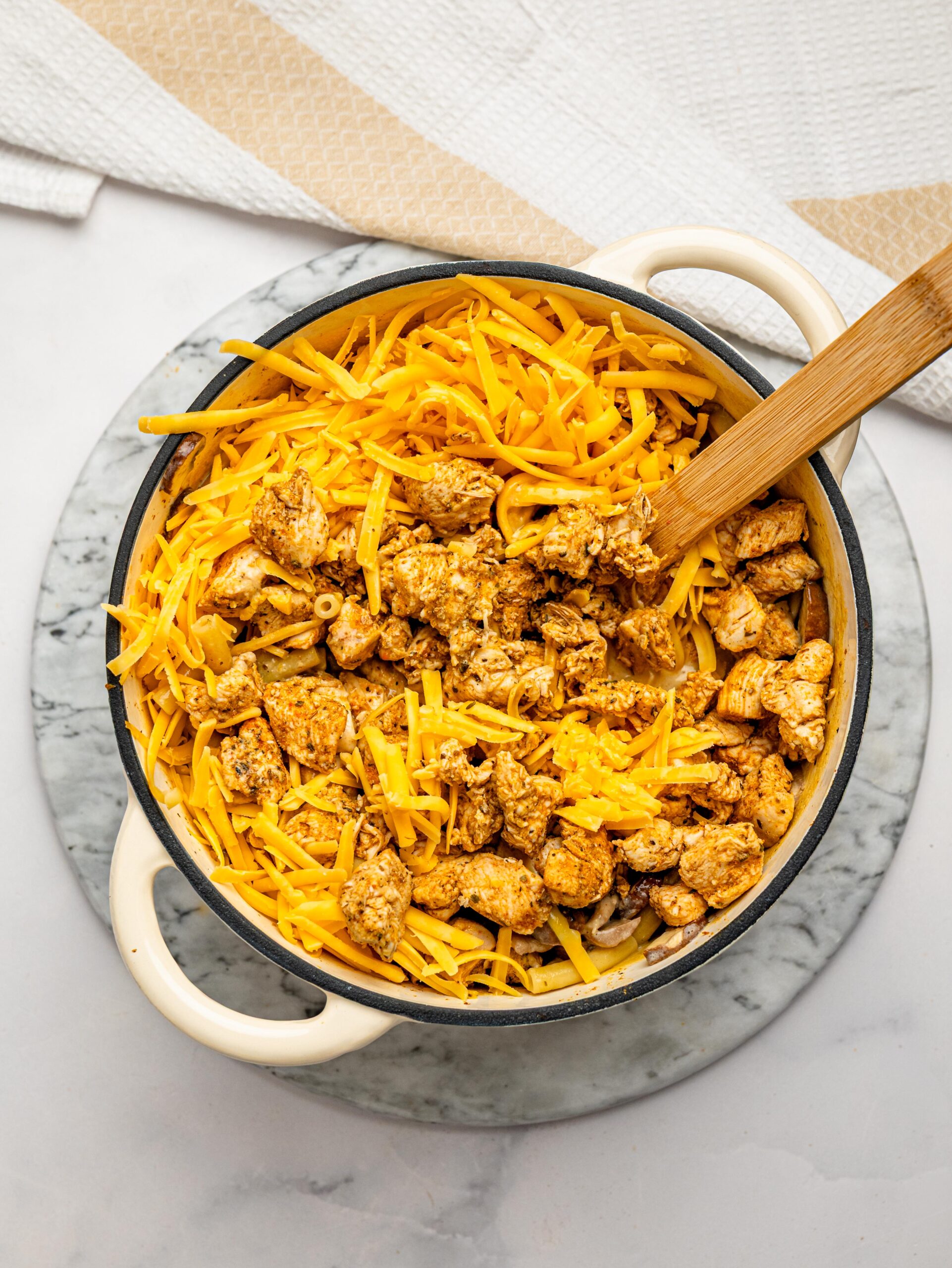 Adding shredded cheese to chicken mac and cheese for a rich and creamy sauce.