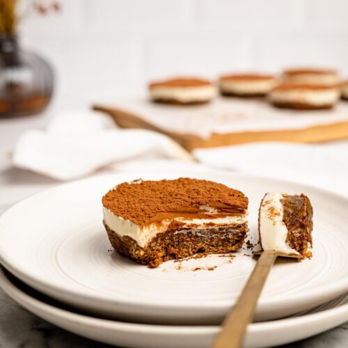 Mini Tiramisu Cheesecake Weetbix Cup with a bite taken out, showing the creamy cheesecake layer and coffee-infused Weetbix base dusted with cocoa powder.