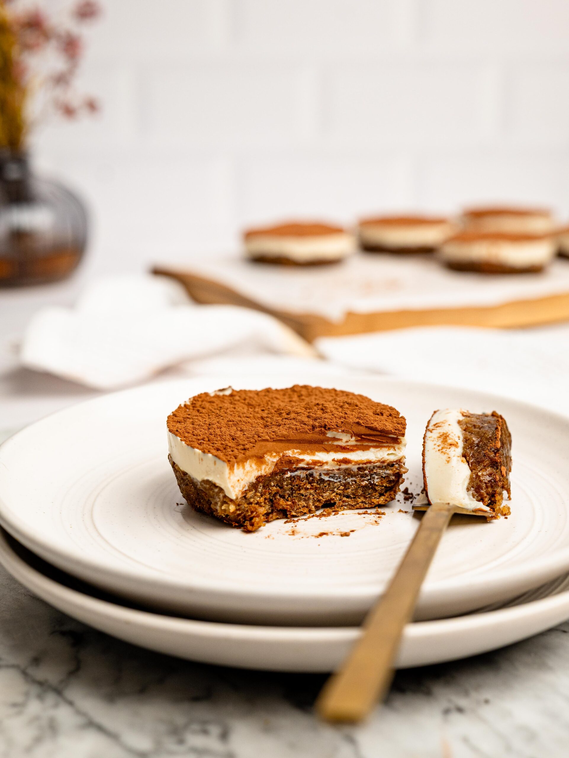 Mini Tiramisu Cheesecake Weetbix Cup with a bite taken out, showing the creamy cheesecake layer and coffee-infused Weetbix base dusted with cocoa powder.