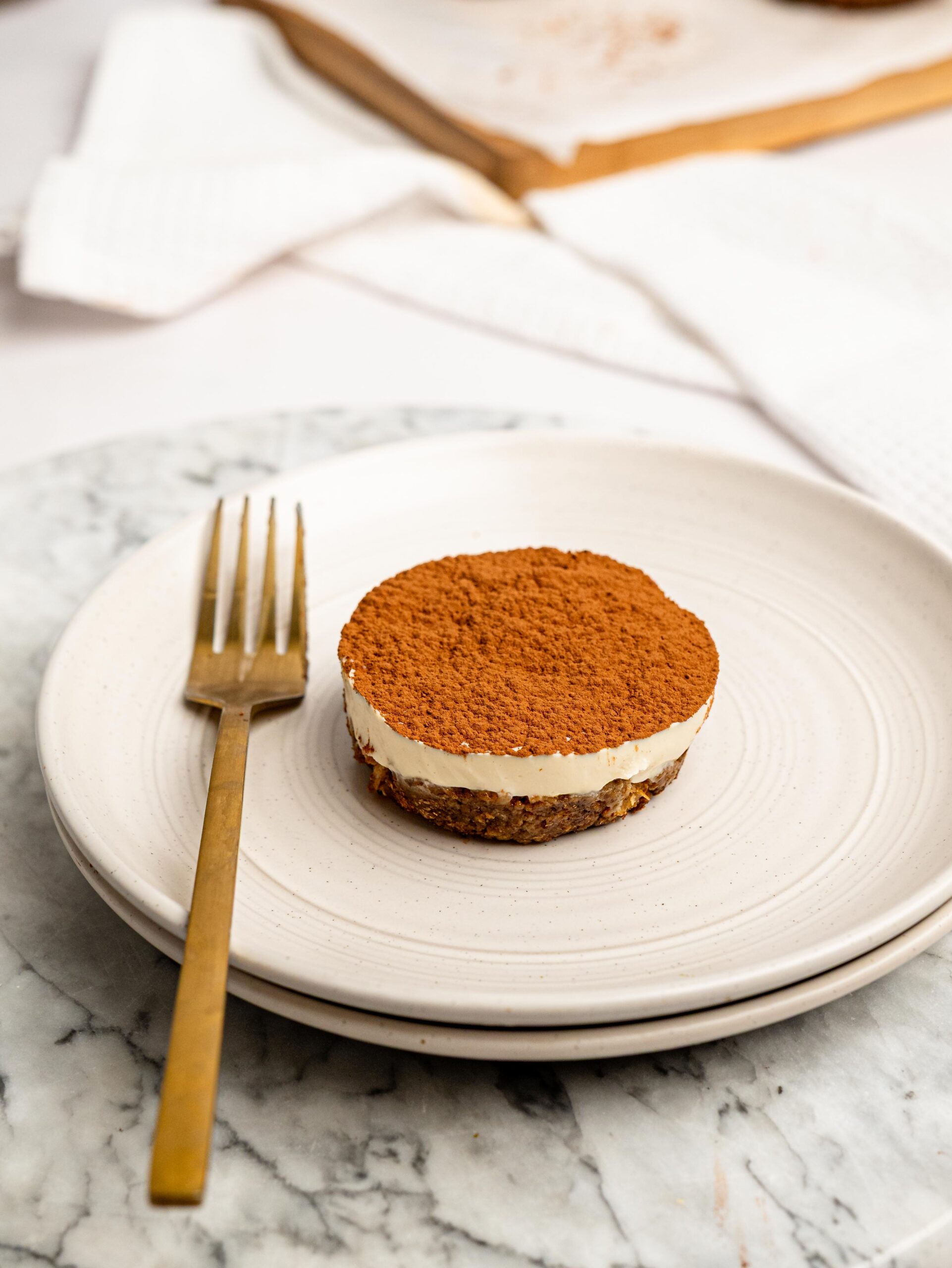 Mini Tiramisu Cheesecake Weetbix Cup dusted with cocoa powder served on a white plate with a gold fork.