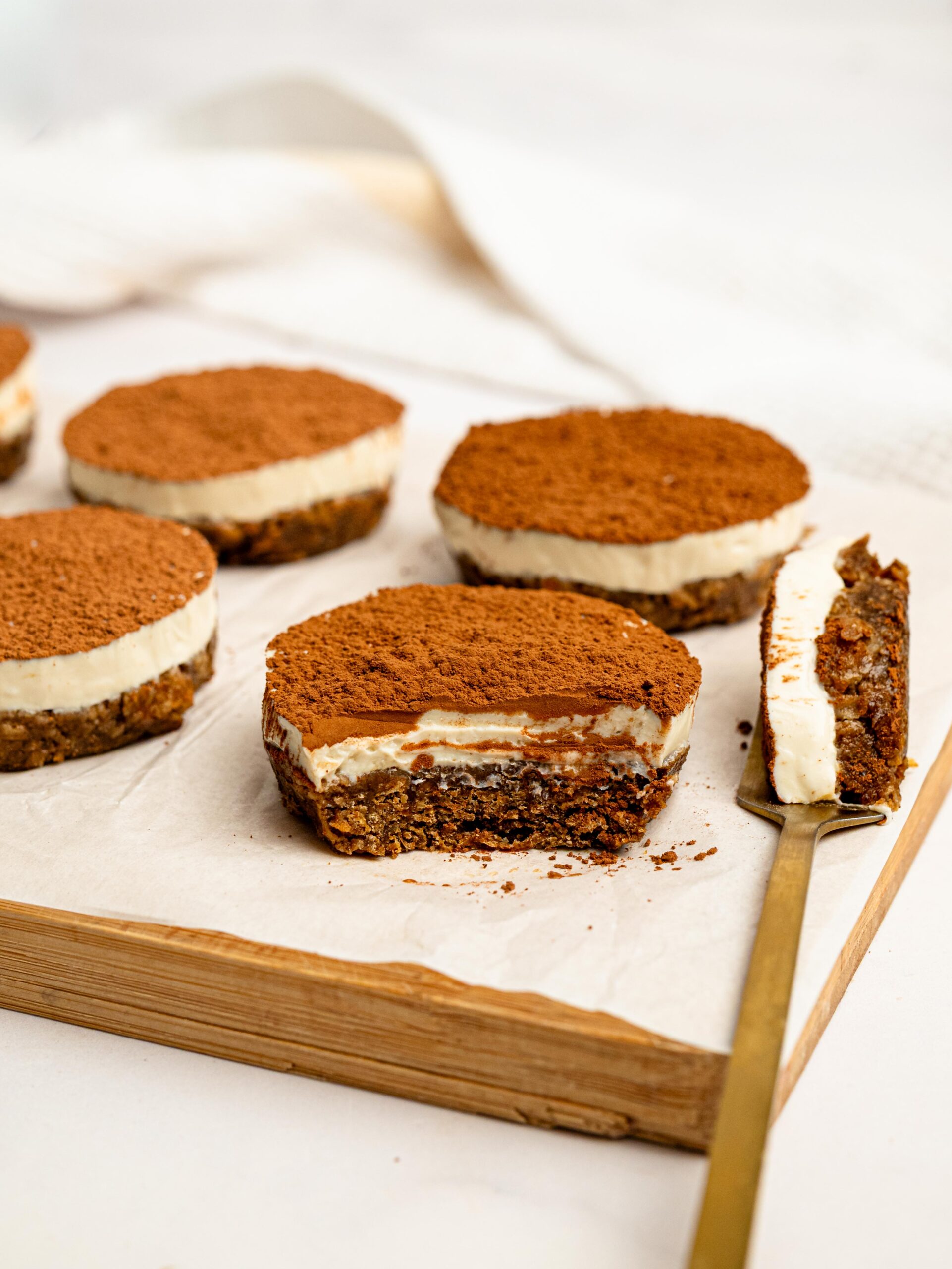 Mini Tiramisu Cheesecake Weetbix Cups on a wooden board with one cup cut open to reveal the creamy cheesecake filling and coffee Weetbix base.