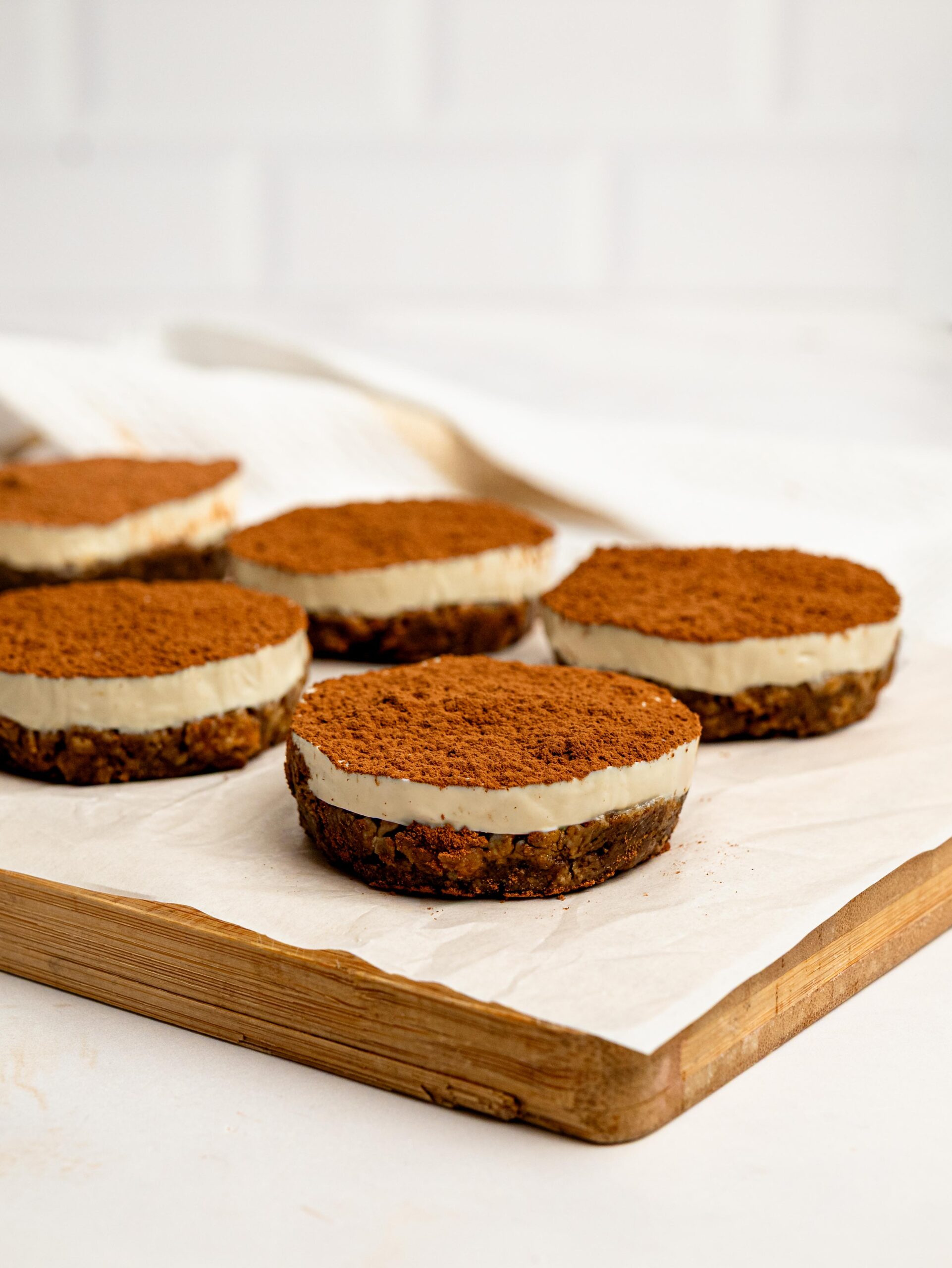 Mini Tiramisu Cheesecake Weetbix Cups arranged on a wooden board with a generous dusting of cocoa powder.