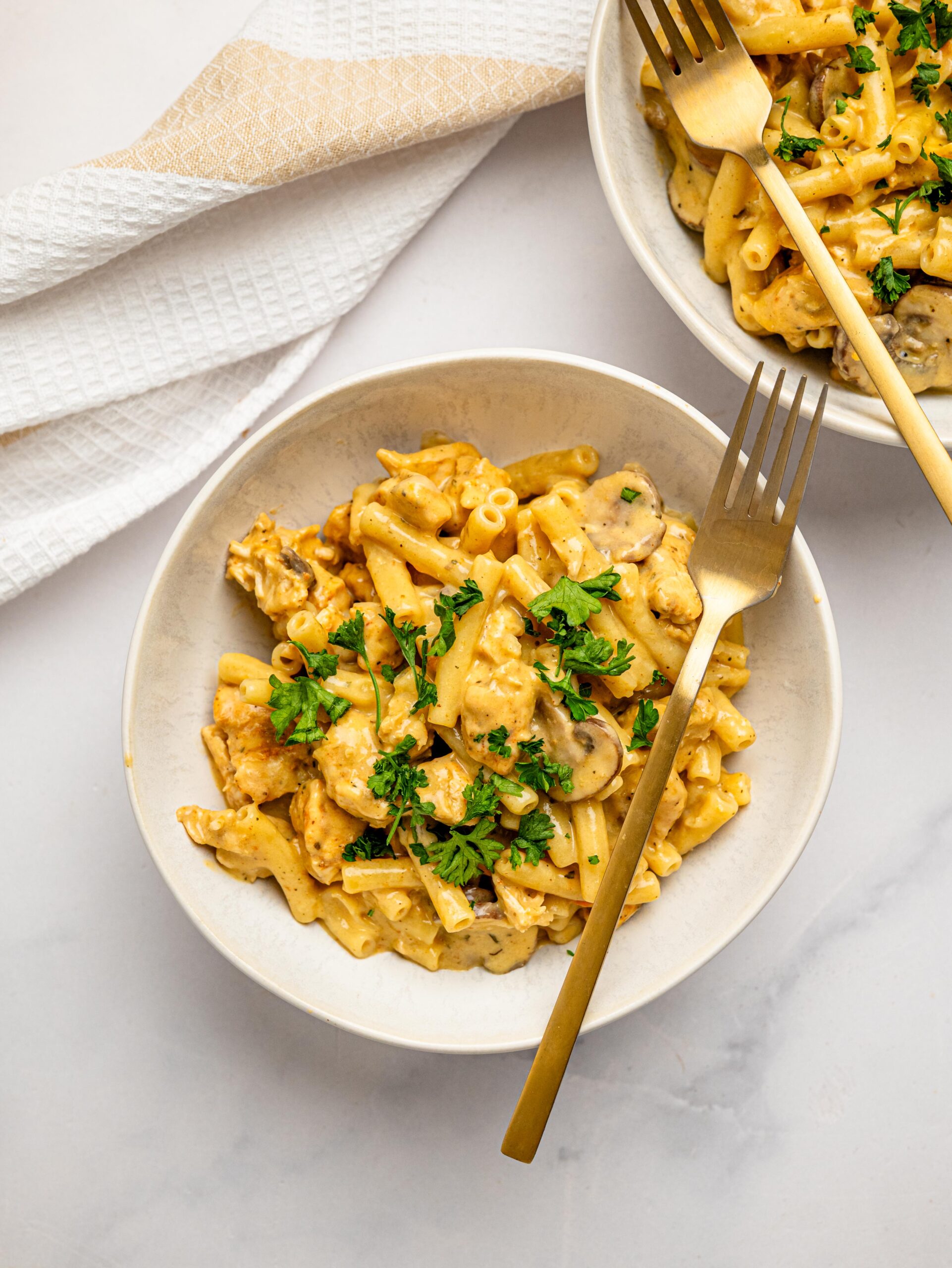 Creamy chicken mac and cheese served in a bowl with mushrooms and fresh parsley.