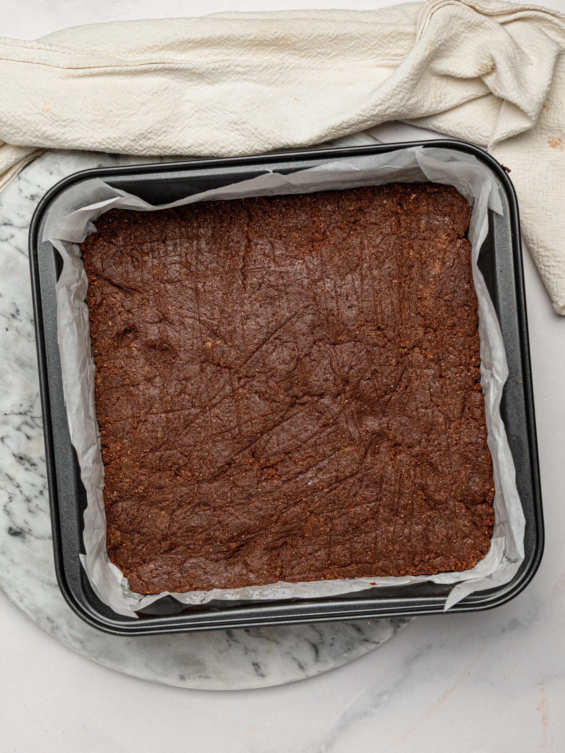 Chocolate protein bar mixture pressed into a parchment-lined baking pan before adding the chocolate topping.