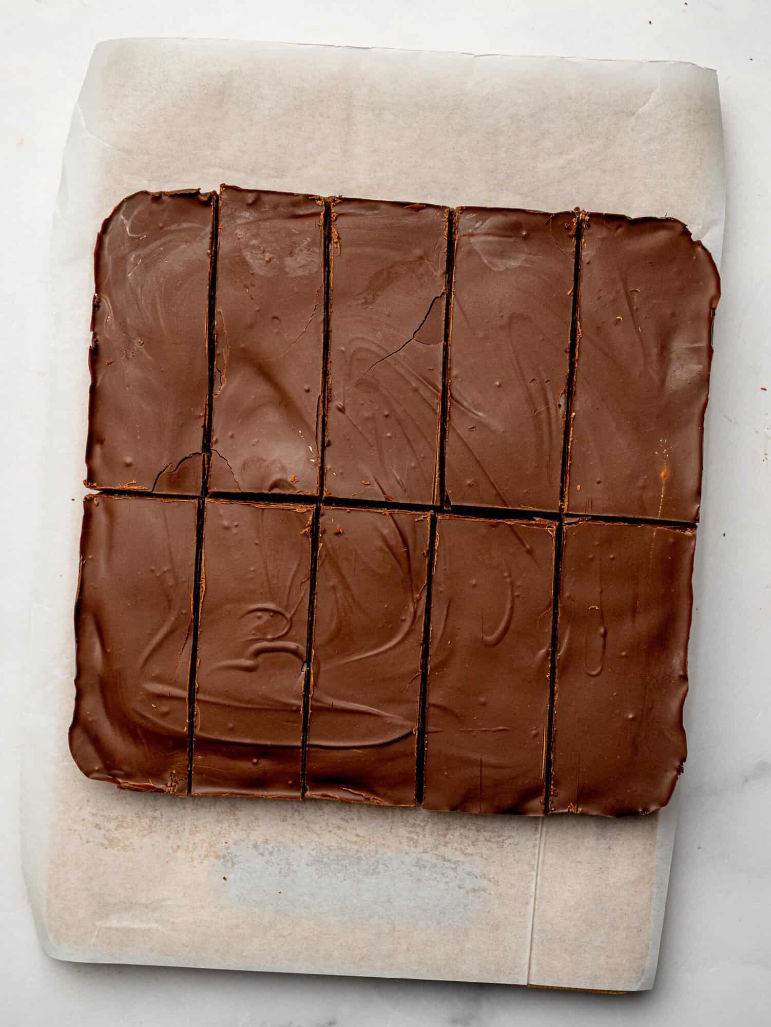 Homemade chocolate protein bars sliced into 10 bars on parchment paper with a dark chocolate topping.