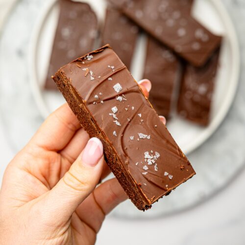 Close-up of a chocolate protein snack bar with a glossy chocolate coating and flaky sea salt.
