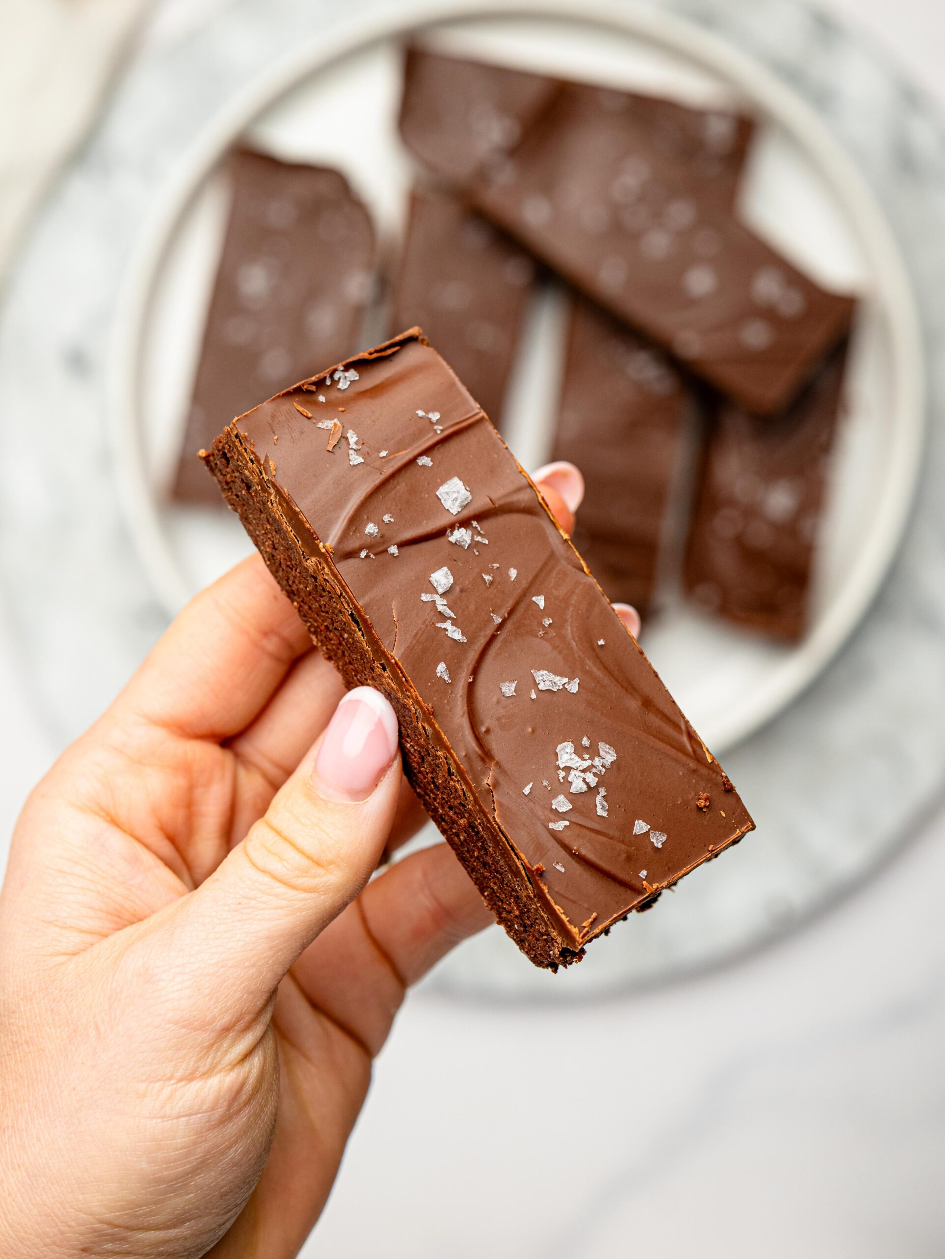 Close-up of a chocolate protein snack bar with a glossy chocolate coating and flaky sea salt.