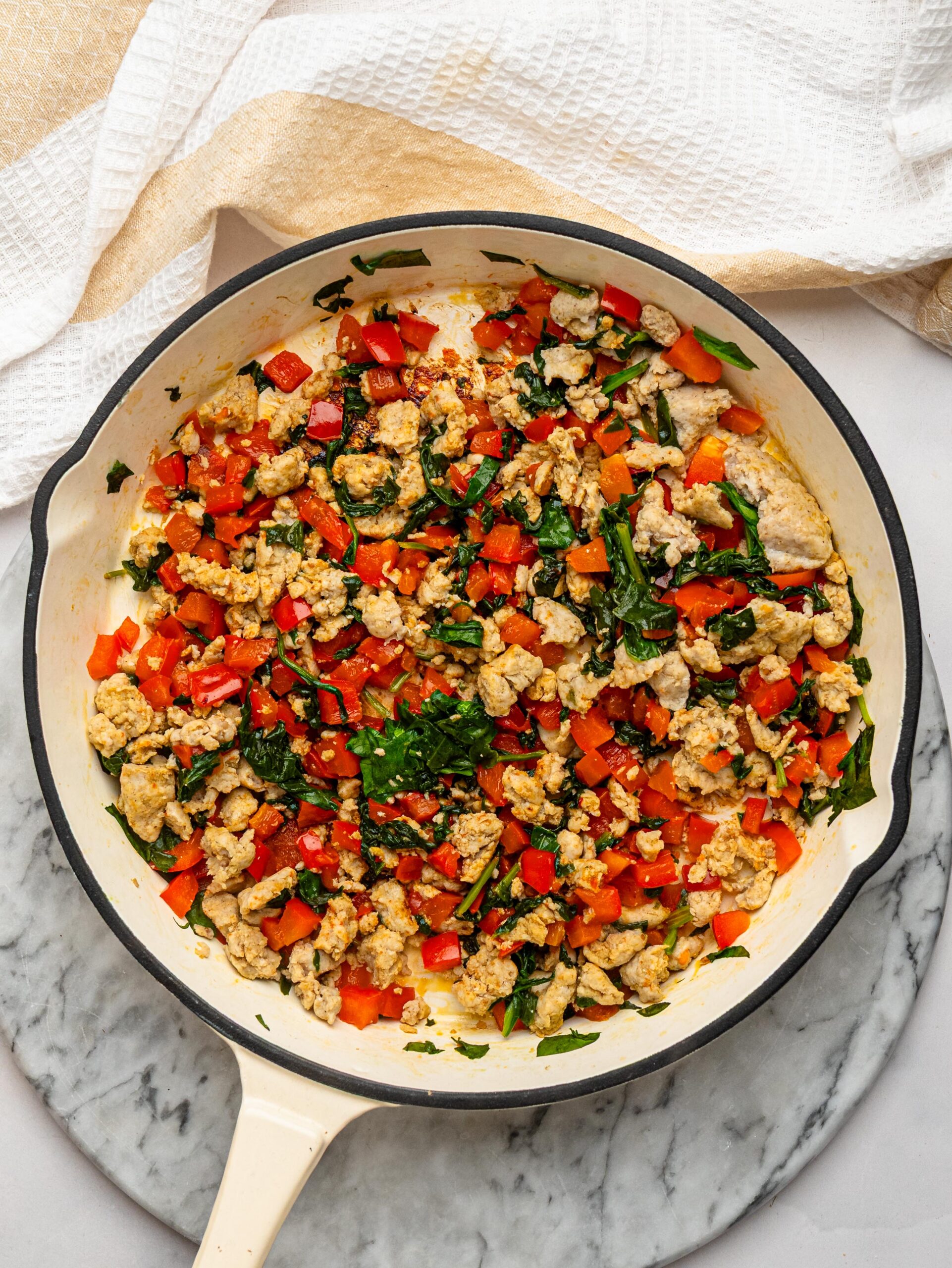Cooked turkey sausage with spinach and diced red bell pepper in a skillet.