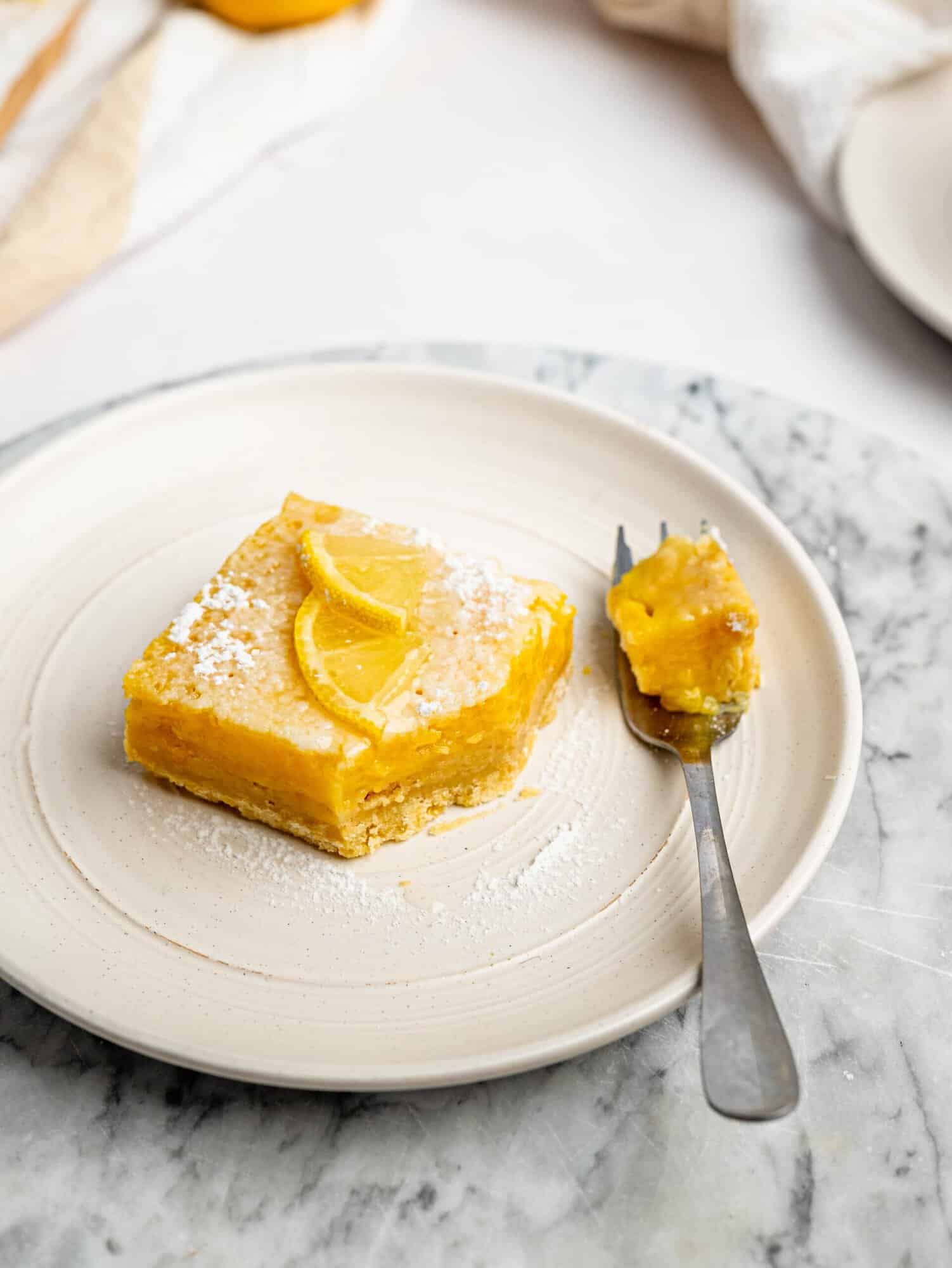 Gluten-free lemon bar dusted with powdered sugar and topped with a lemon slice.