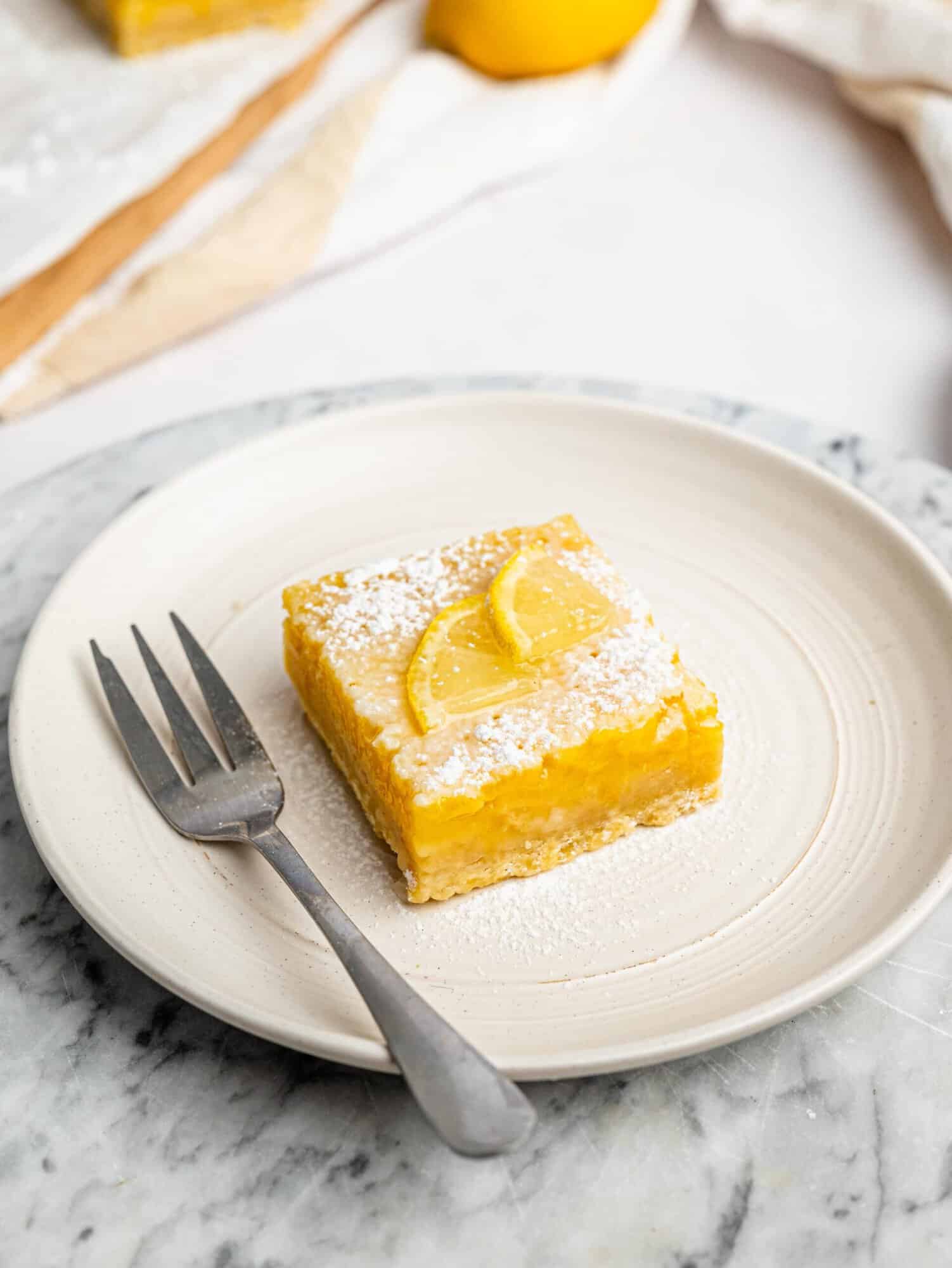 Gluten-free lemon bar dusted with powdered sugar and topped with fresh lemon slices.