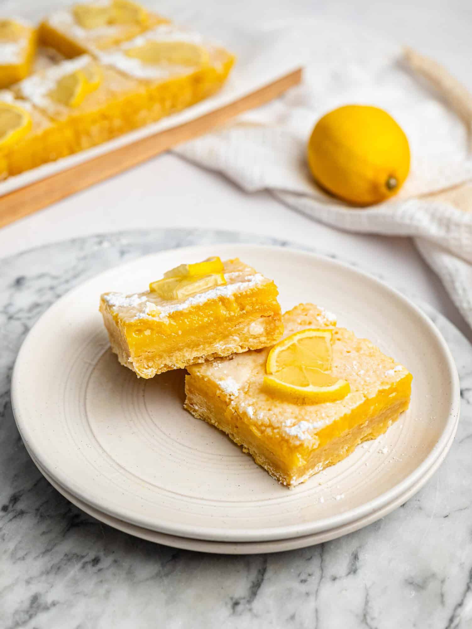 Gluten-free lemon bars served on a plate with lemon slices and powdered sugar.