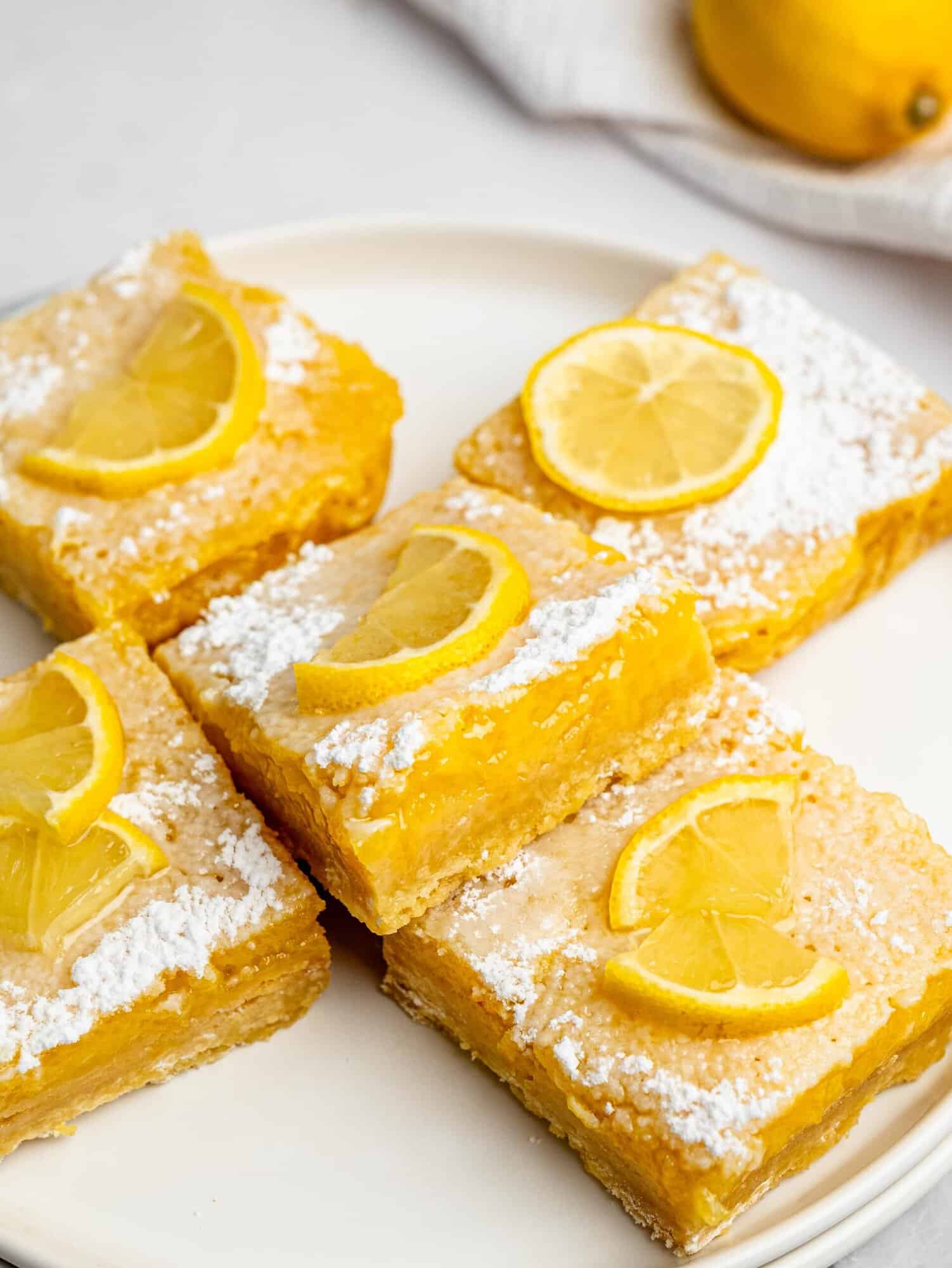 Plate of gluten-free lemon bars topped with powdered sugar and fresh lemon slices.