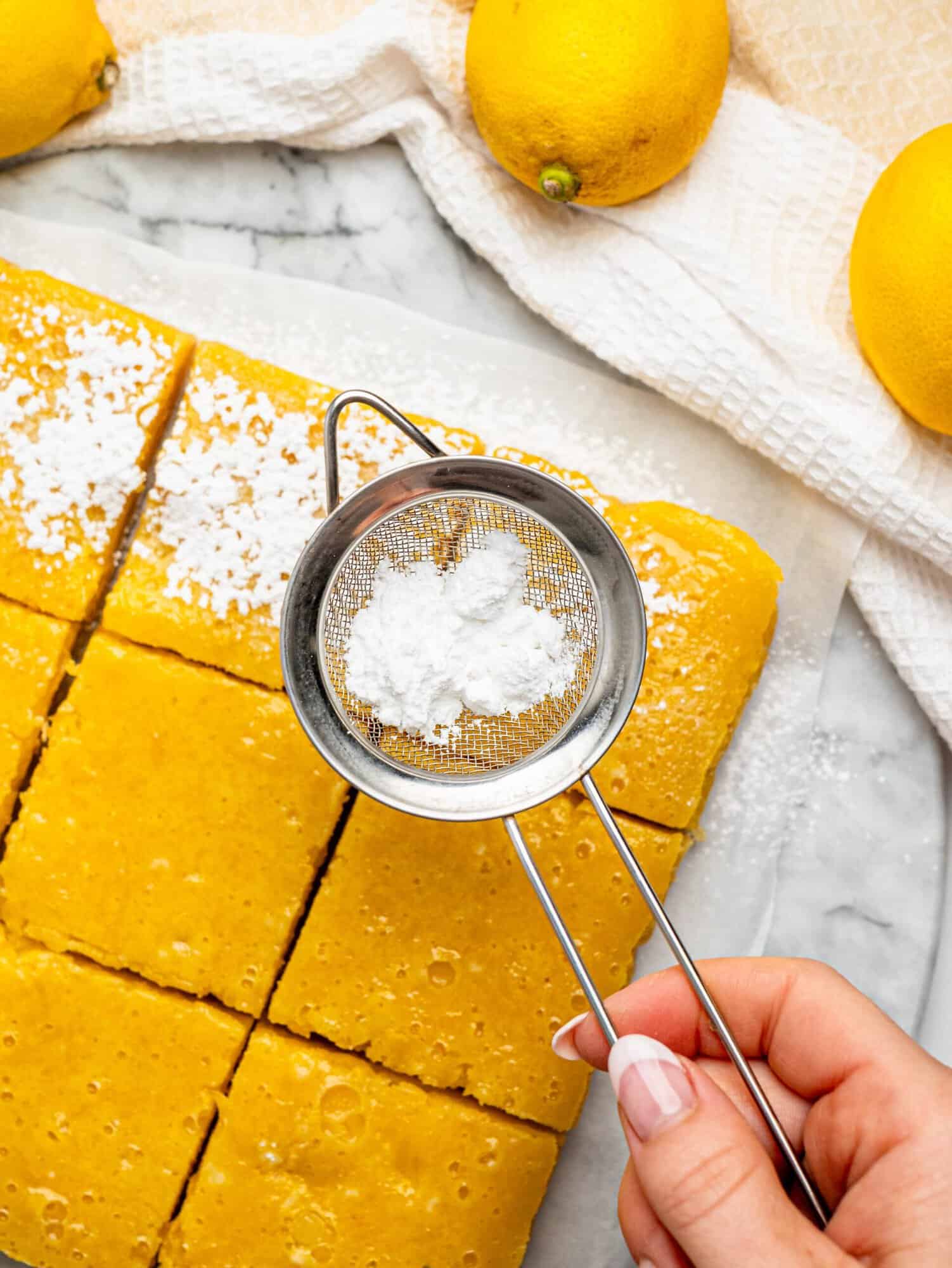 Gluten free lemon bars being dusted with powdered sugar.