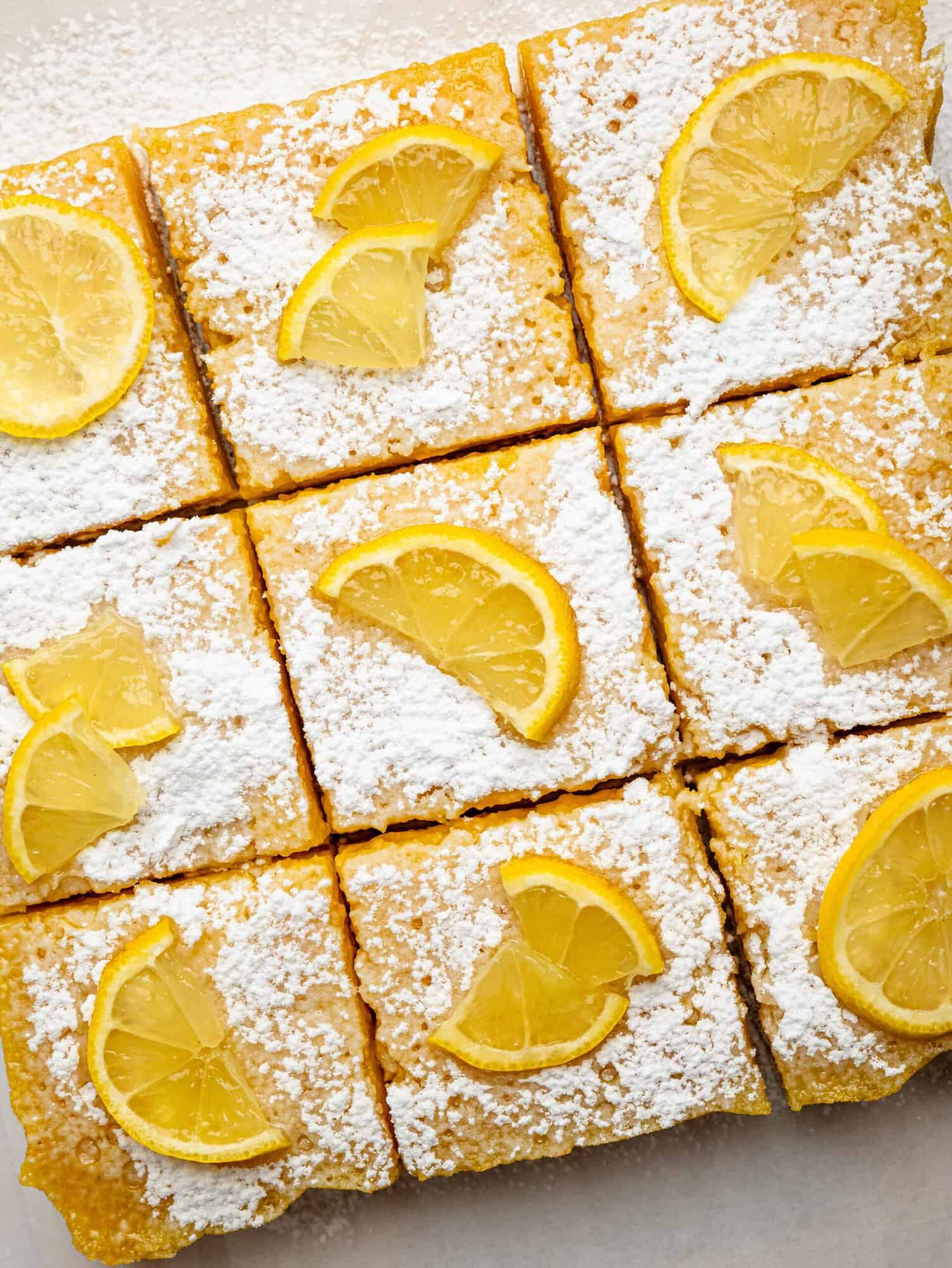 Top view of gluten-free lemon bars arranged on parchment paper with lemon slices.