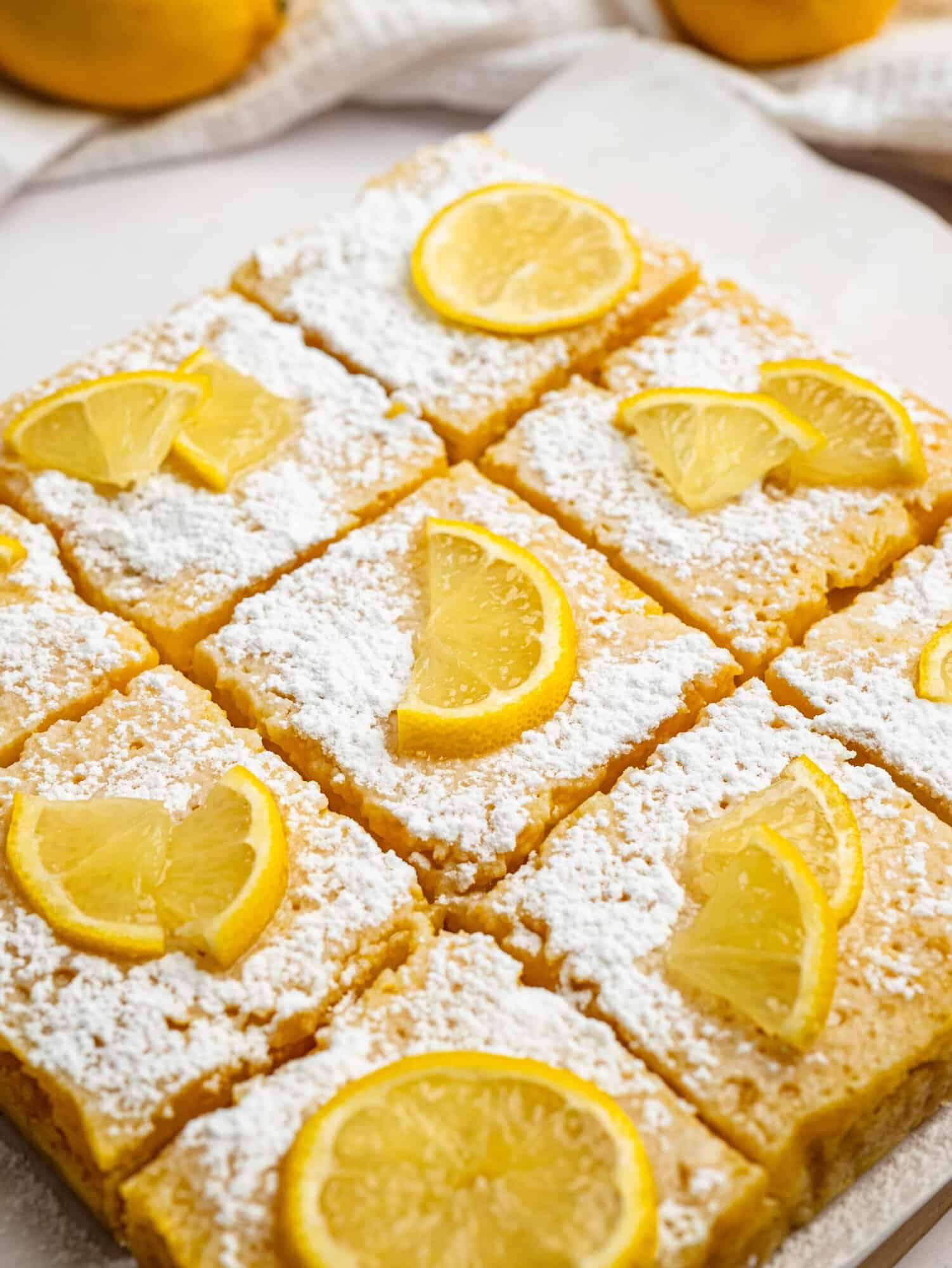 Homemade gluten-free lemon bars cut into squares and topped with powdered sugar and lemon slices.