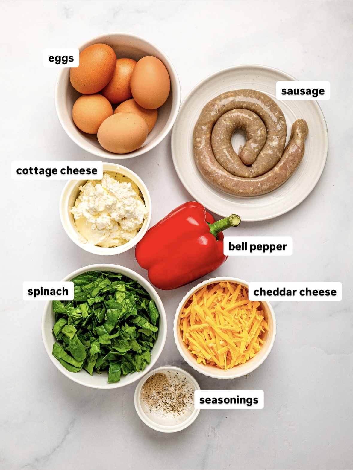 Ingredients for a high protein egg bake including eggs, cottage cheese, sausage, spinach, bell pepper and cheddar.