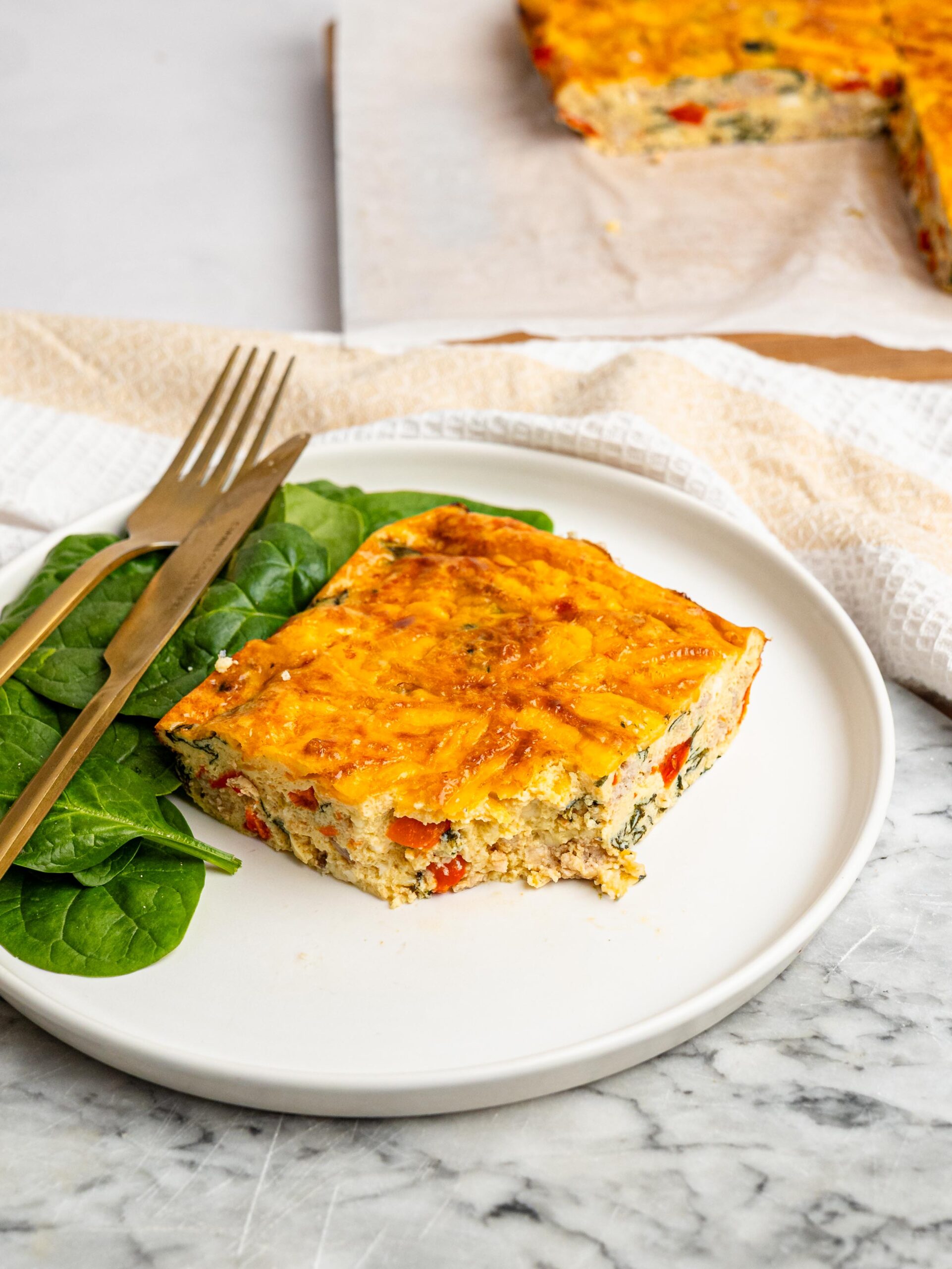 Slice of high protein egg bake with cottage cheese served with spinach.