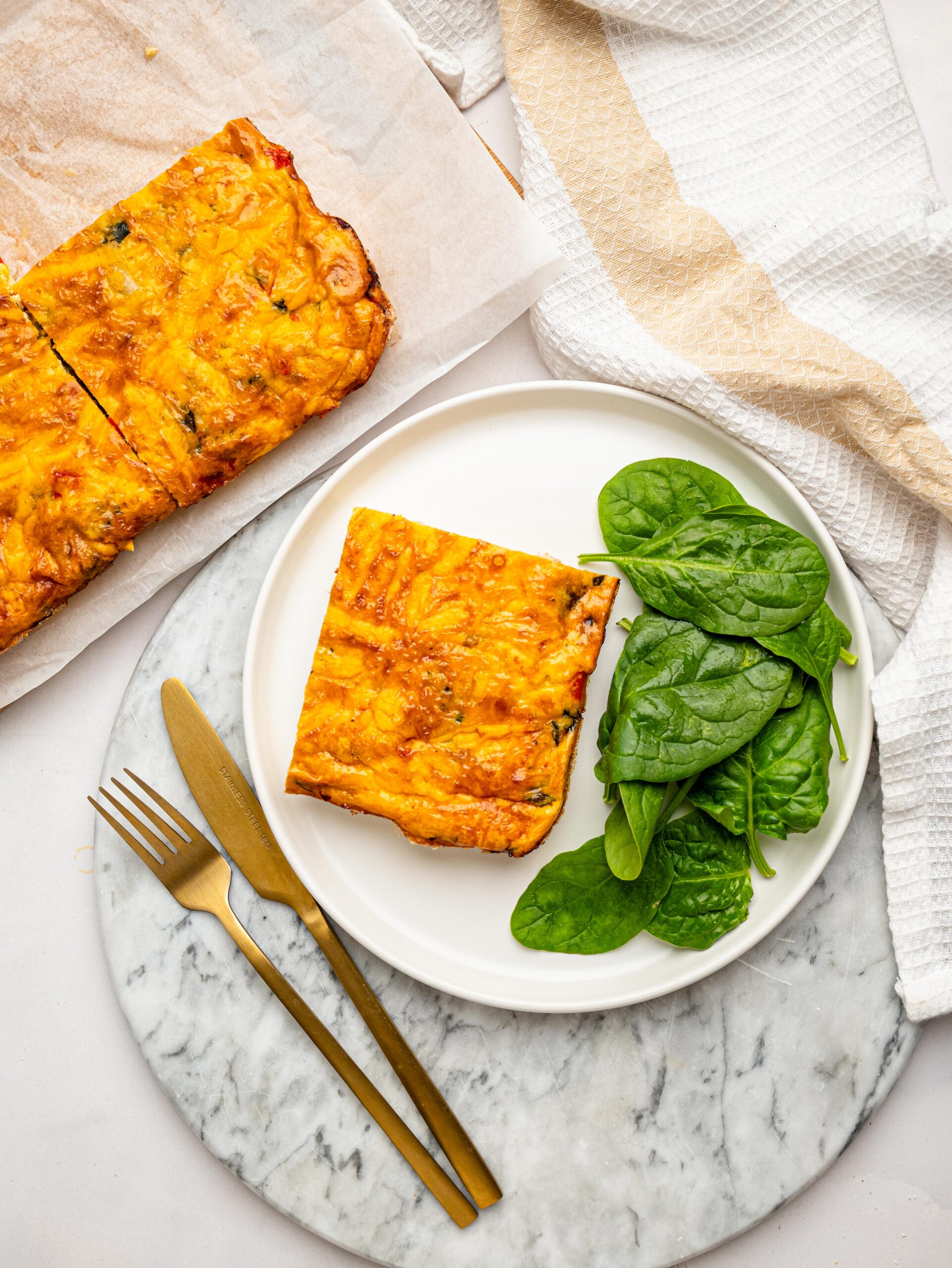 High protein egg bake portion served with spinach alongside the remaining egg bake.