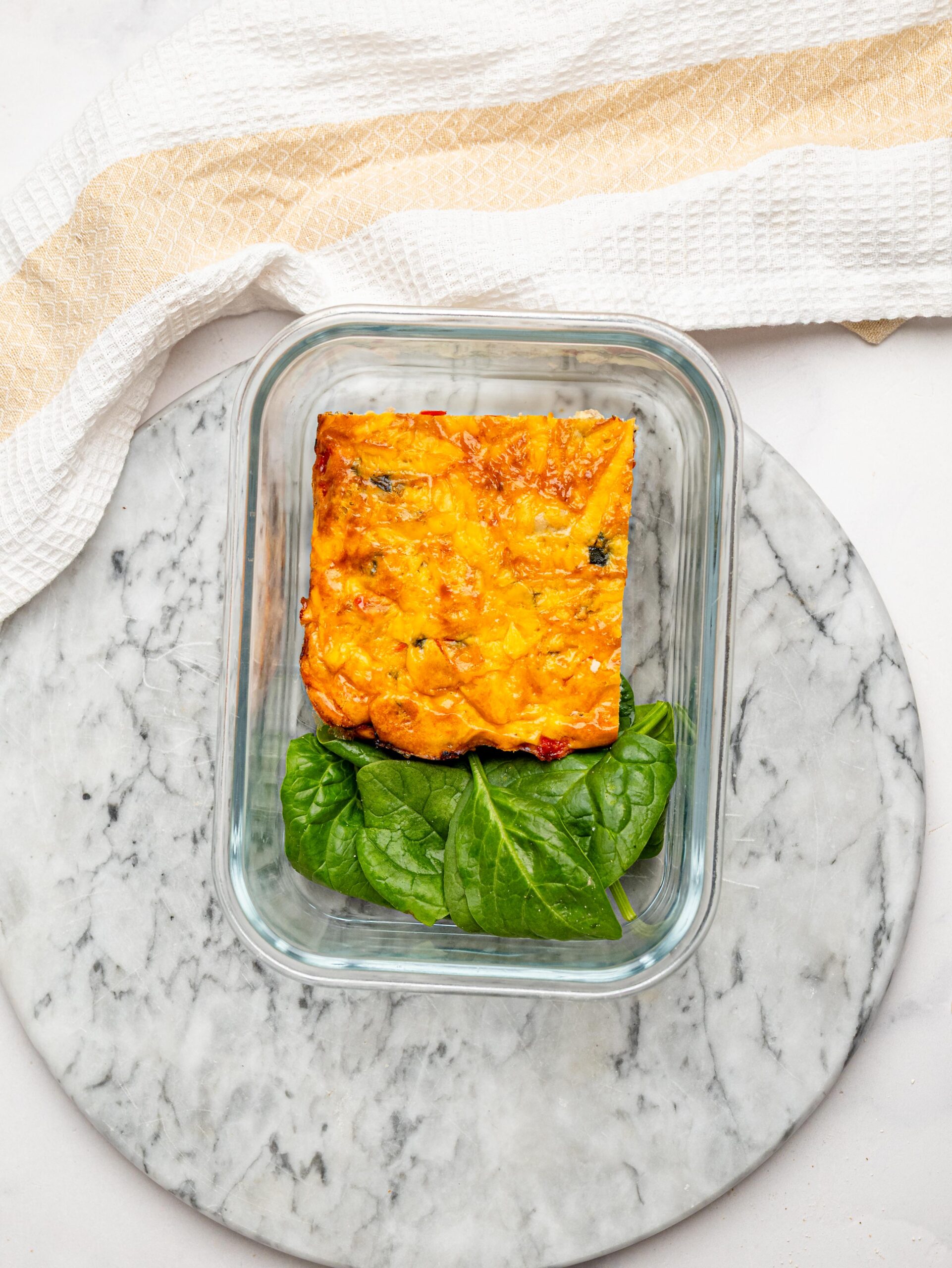 High protein egg bake portion stored in a glass container with fresh spinach.