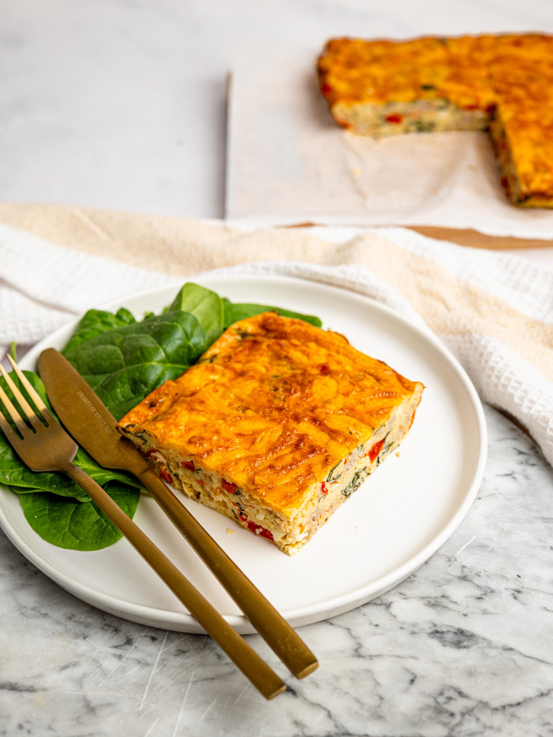 Slice of high protein egg bake with cottage cheese served with spinach.