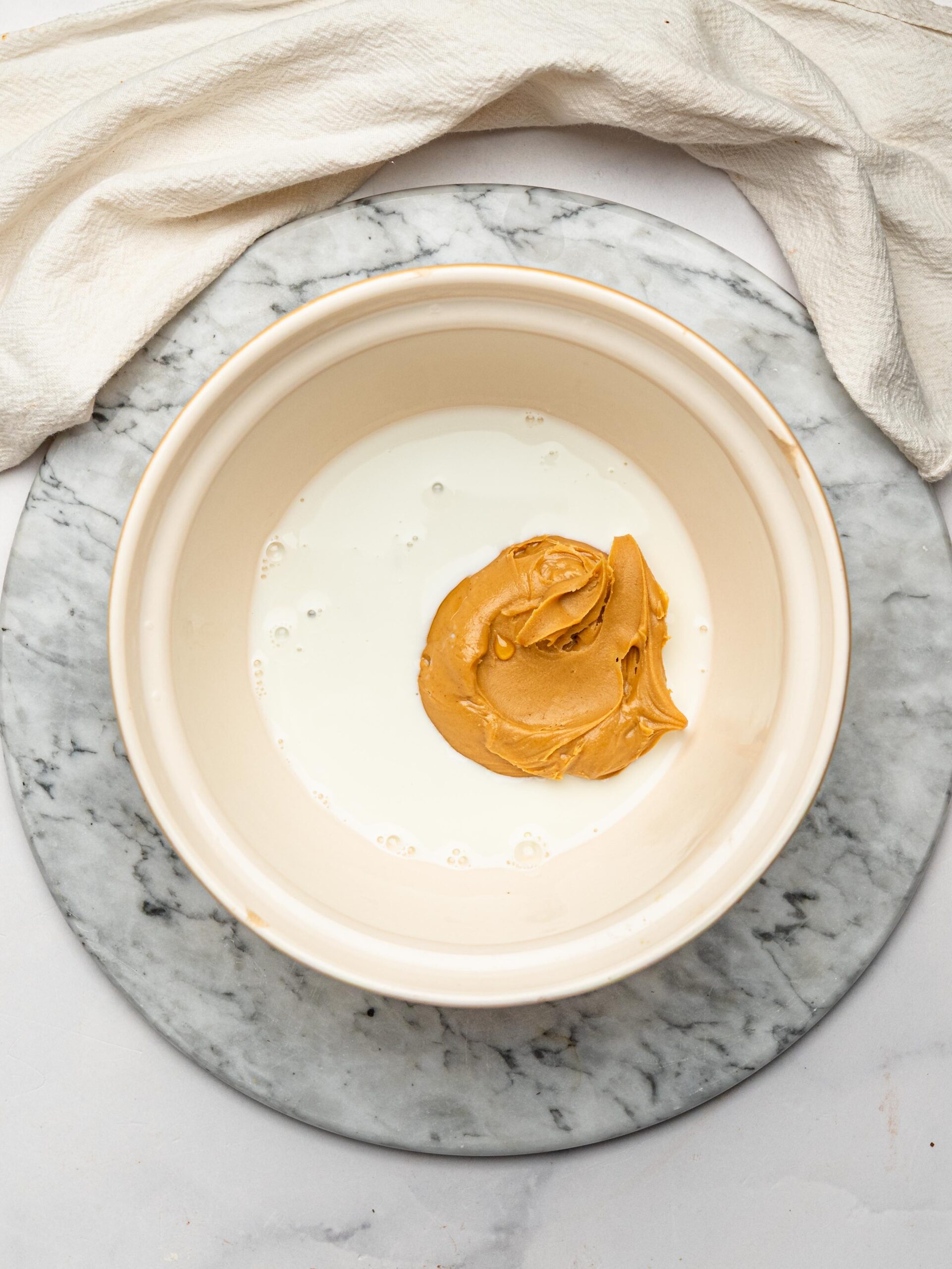 Natural peanut butter, honey, and milk in a mixing bowl before making homemade chocolate protein bars.