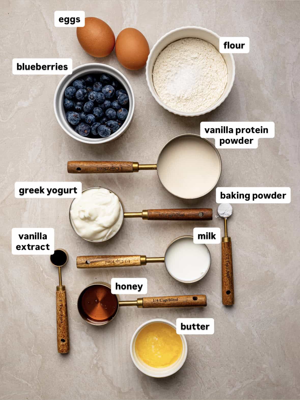 Ingredients for high protein blueberry muffins including eggs, flour, Greek yogurt, blueberries, honey and milk.
