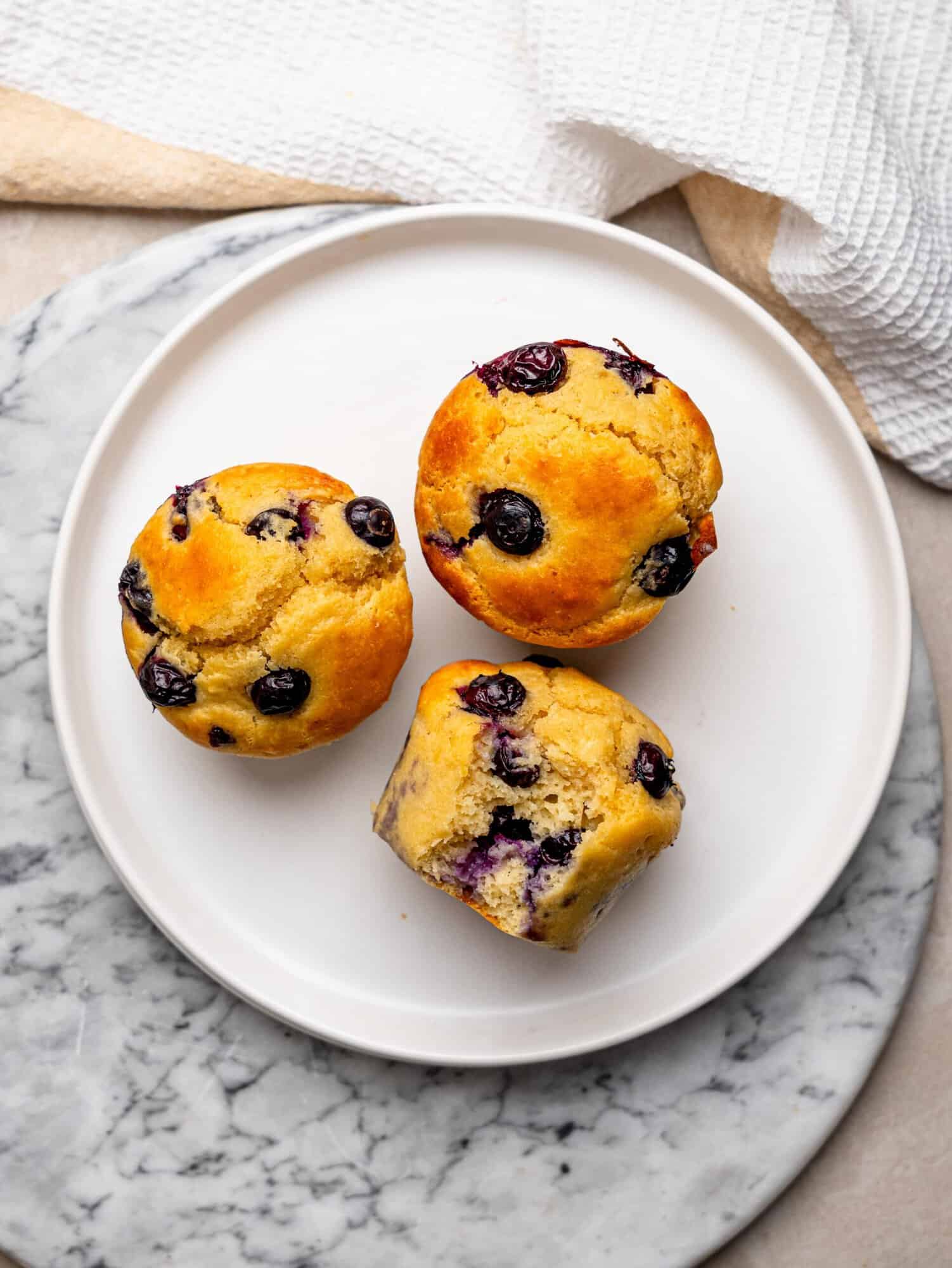 Overhead view of three blueberry protein muffins arranged on a white plate.