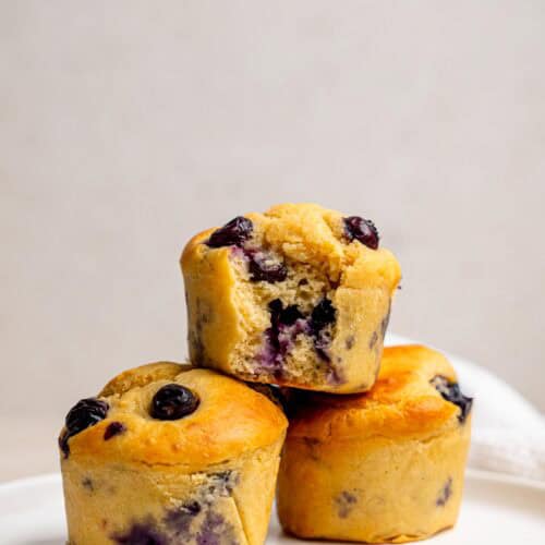 High protein blueberry muffin recipe with three golden muffins and one cut open to show the soft blueberry-filled centre.