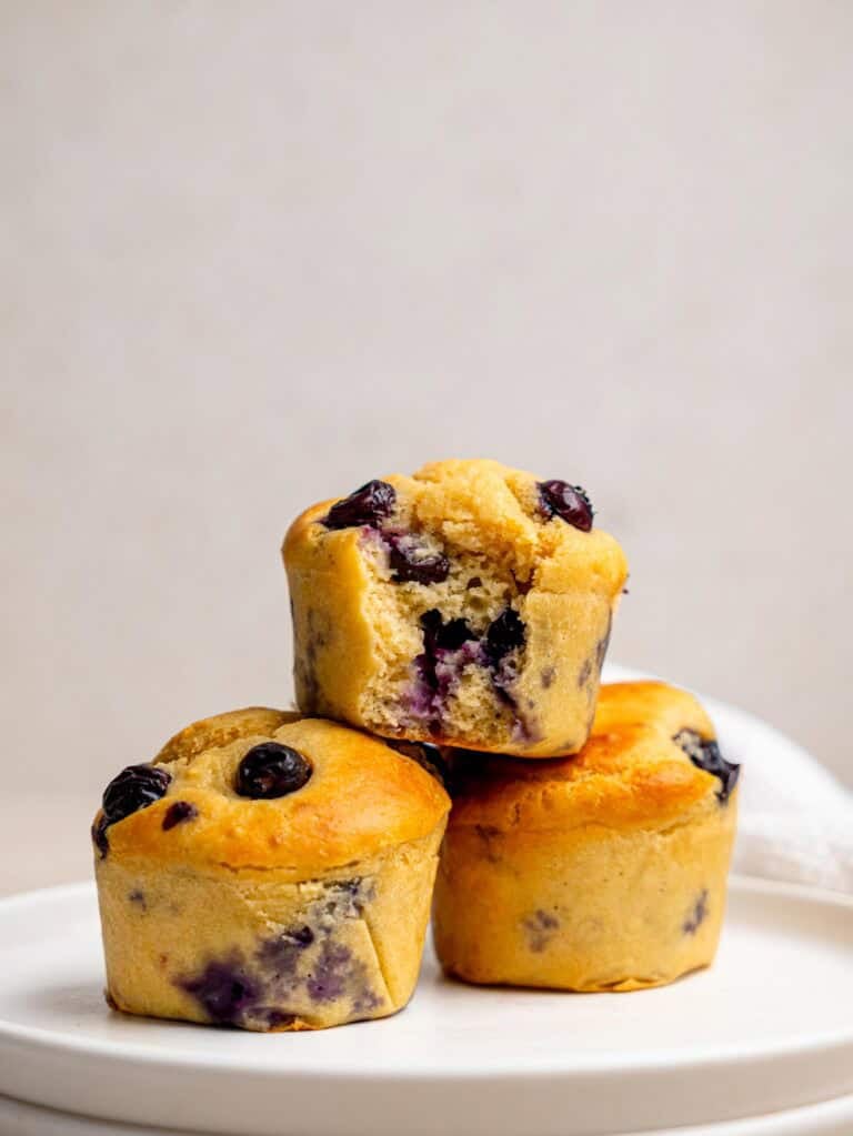 High protein blueberry muffin recipe with three golden muffins and one cut open to show the soft blueberry-filled centre.