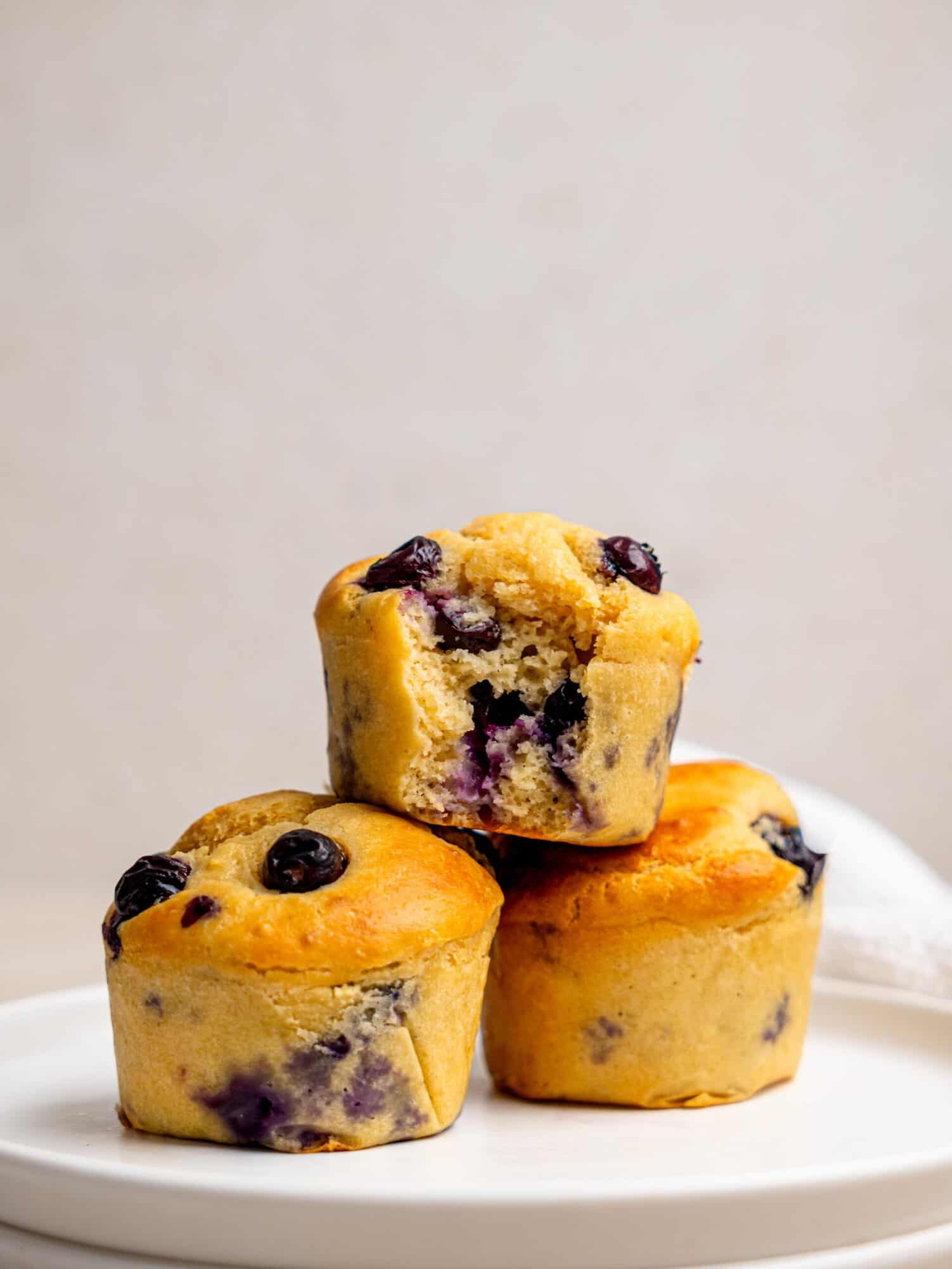 High protein blueberry muffin recipe with three golden muffins and one cut open to show the soft blueberry-filled centre.