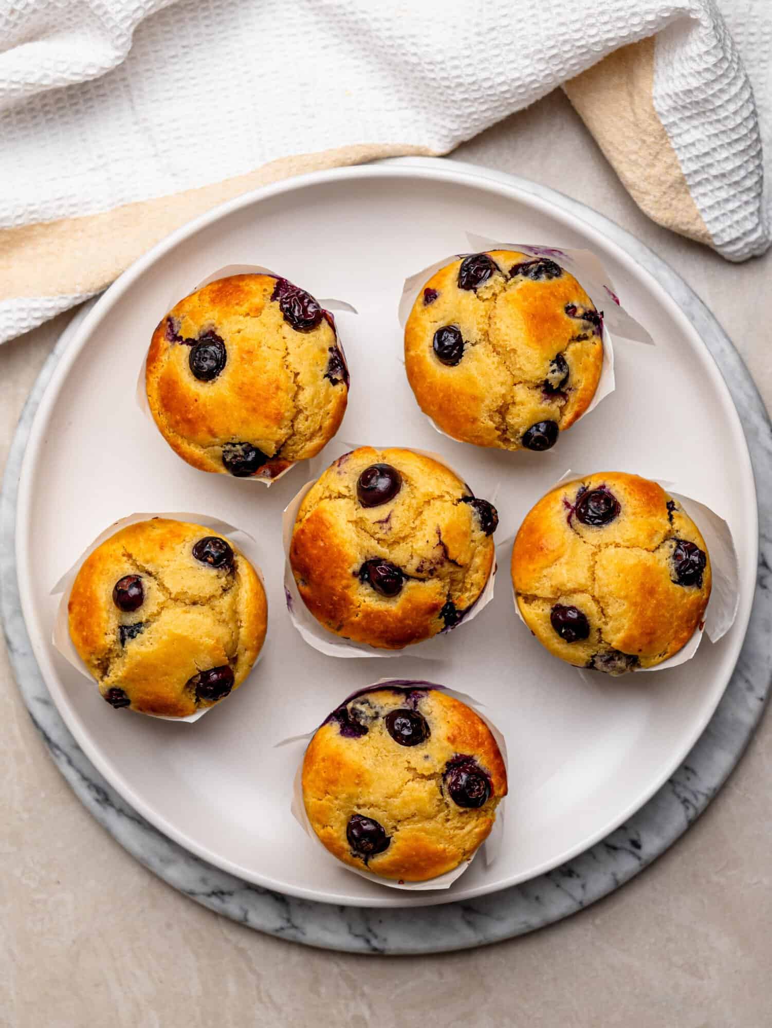 Six golden high protein blueberry muffins arranged on a white plate.