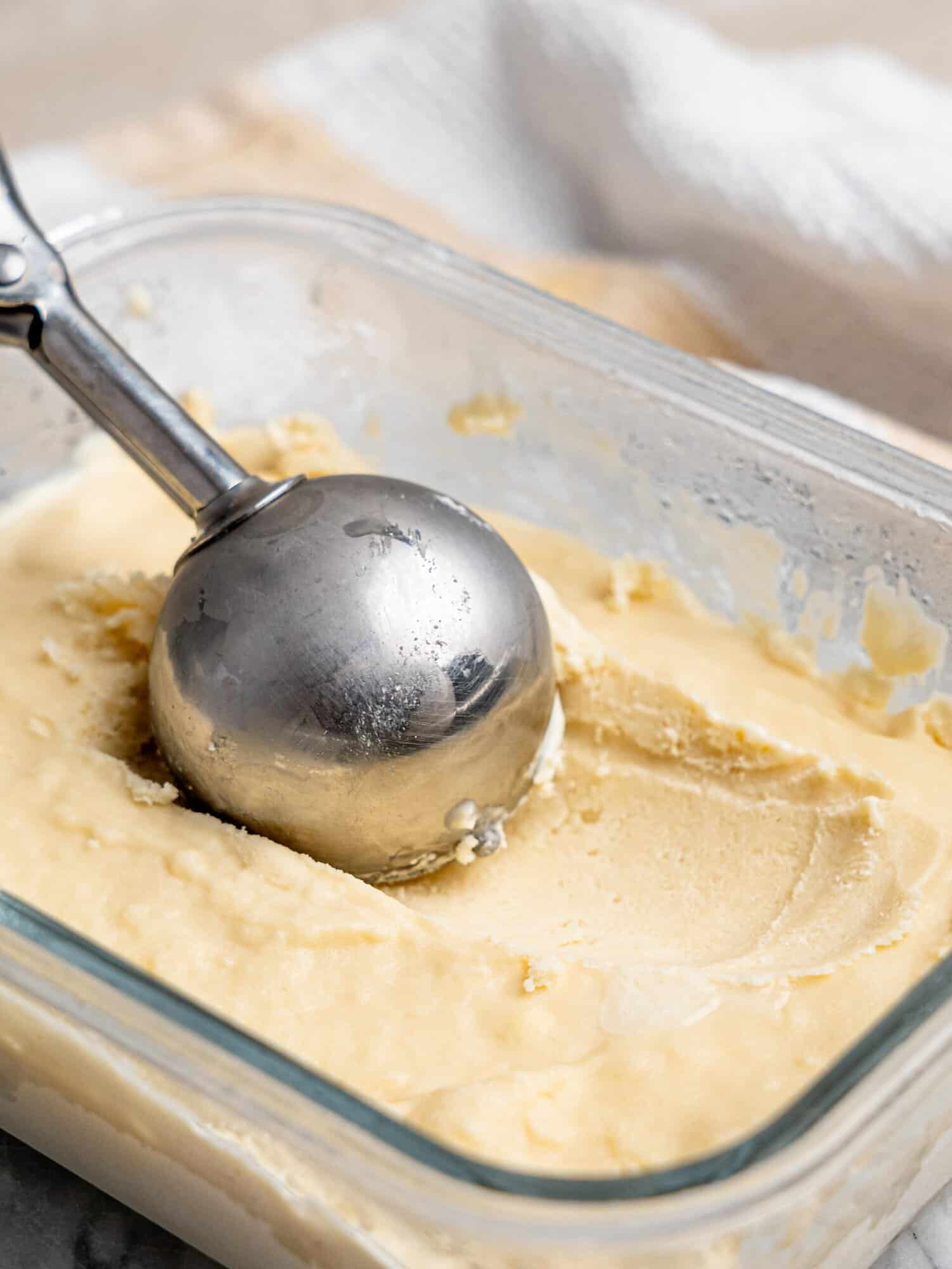 Ice cream scoop pressing into creamy cottage cheese ice cream in a glass container.