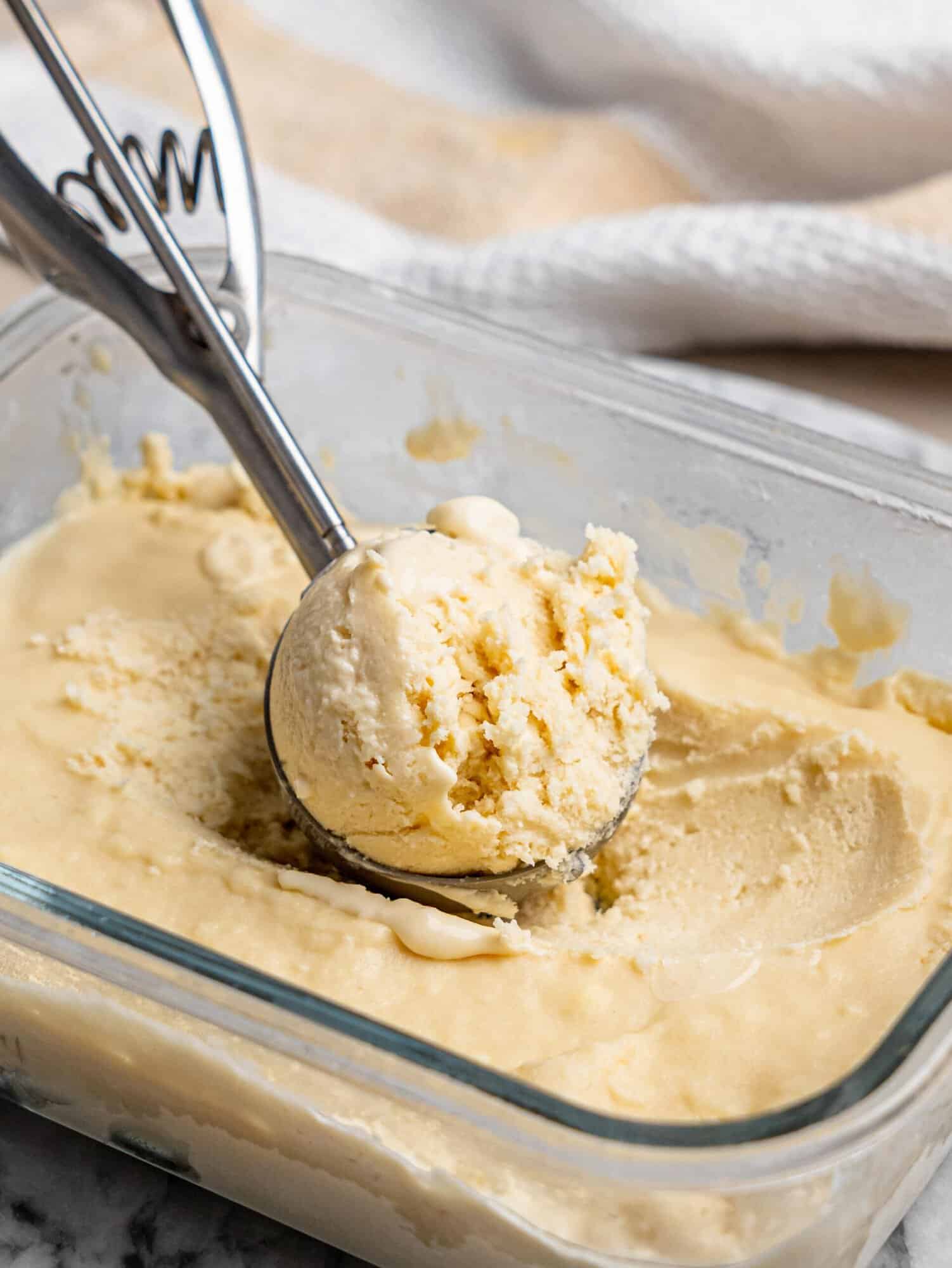 A scoop of creamy protein ice cream being served from a freezer container.